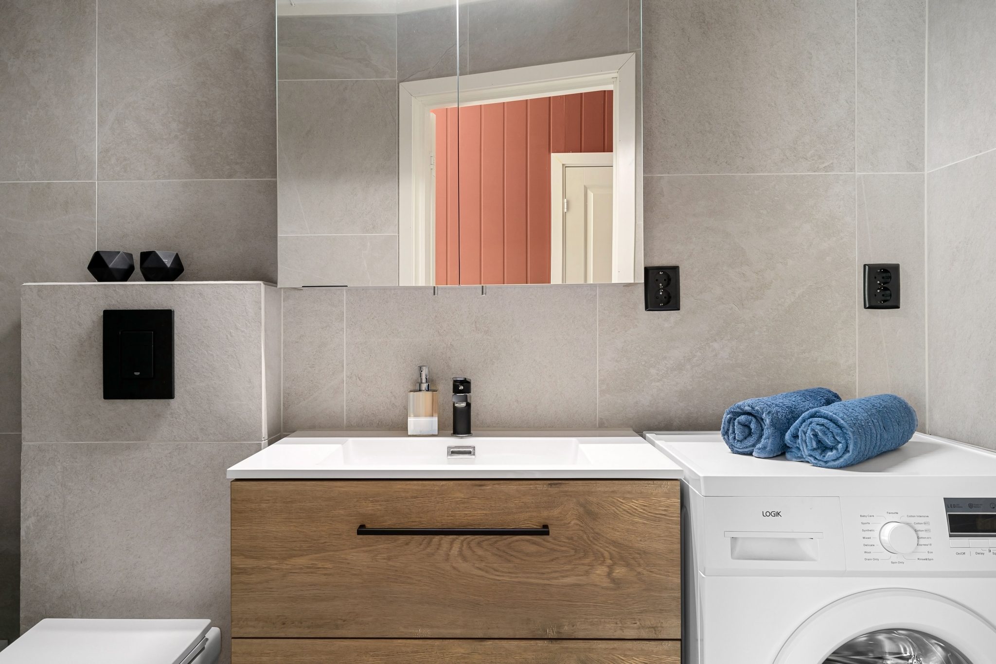 Contemporary bathroom featuring a sleek wooden vanity, washing machine, and modern fixtures.