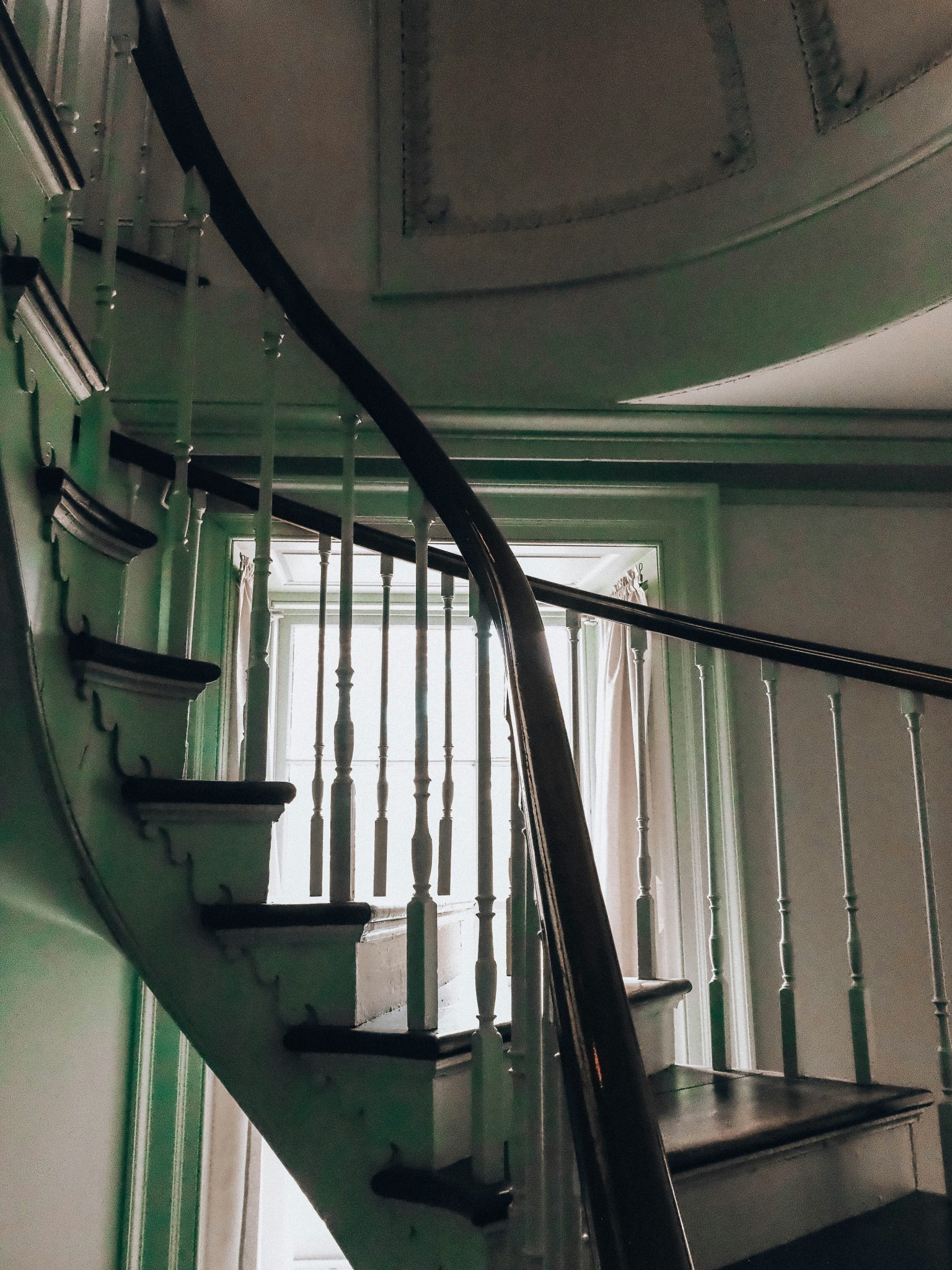 Elegant curved wooden staircase with white balusters and green walls.