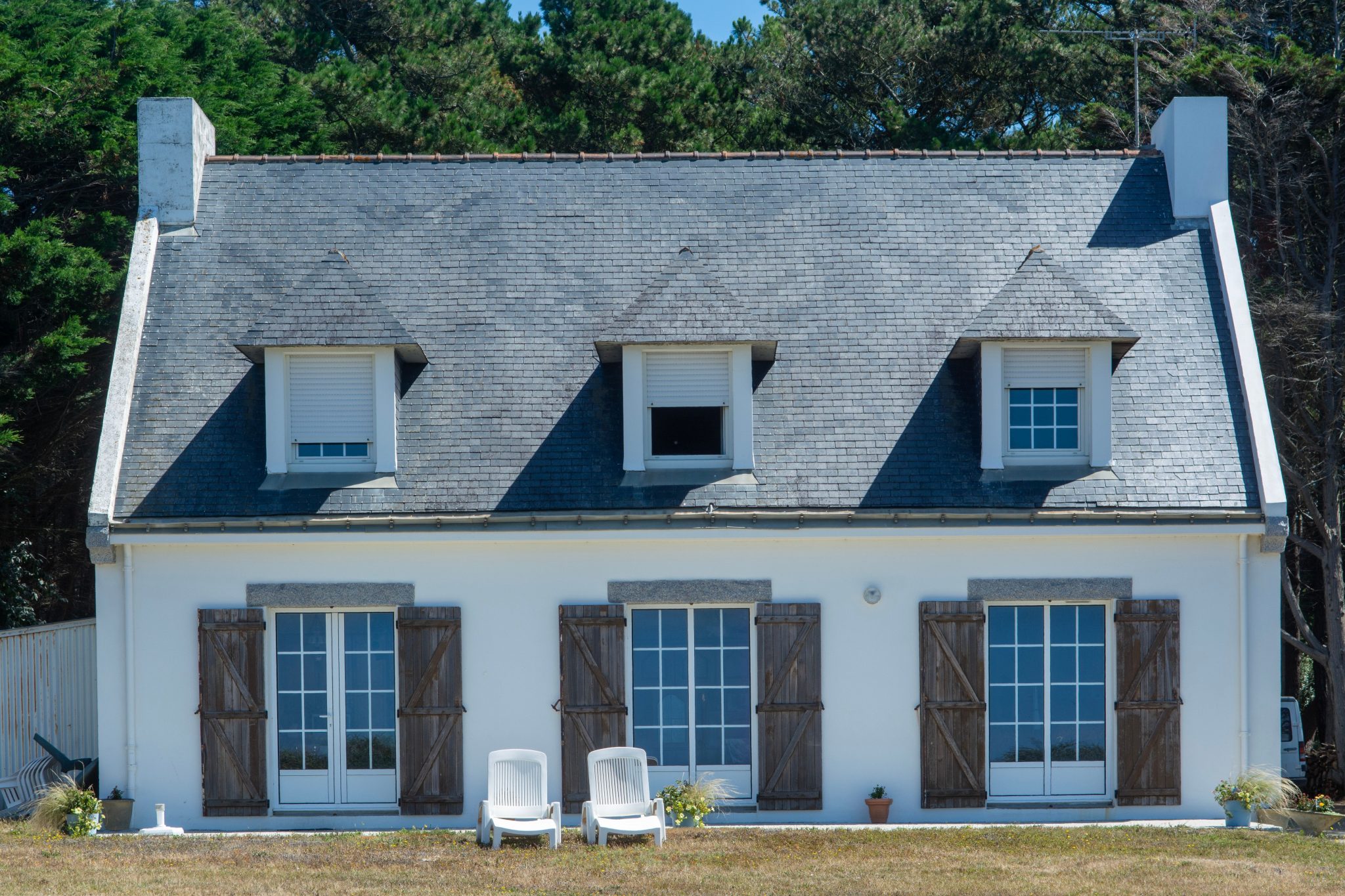 Elegant French cottage with slate roof, wooden shutters, and a peaceful garden setting.
