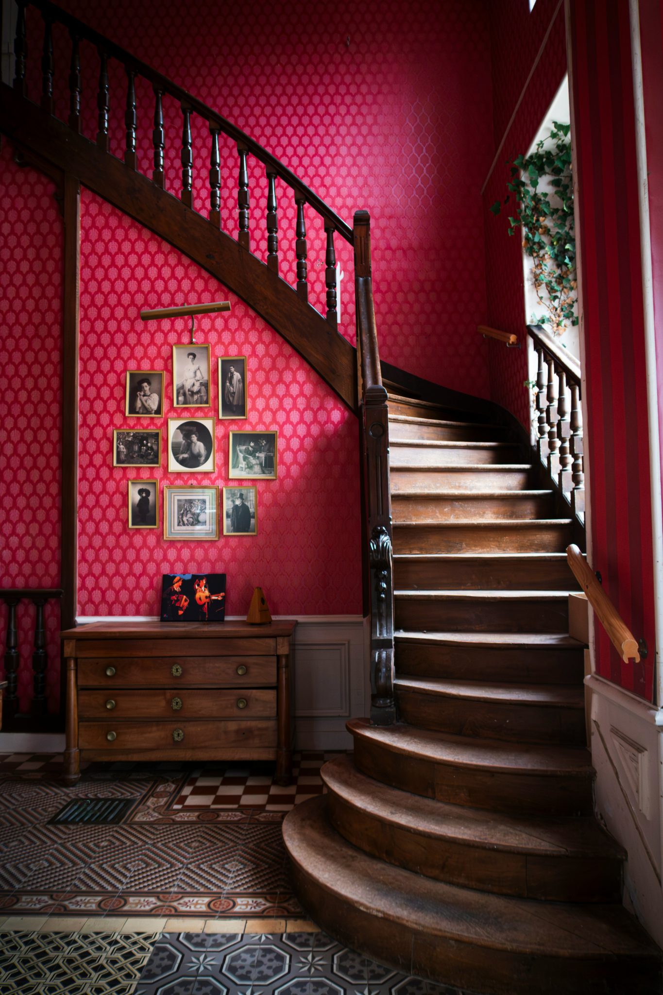 Elegant interior of a French country house hallway with a vintage wooden staircase, patterned wallpaper, antique furniture, and historic charm.