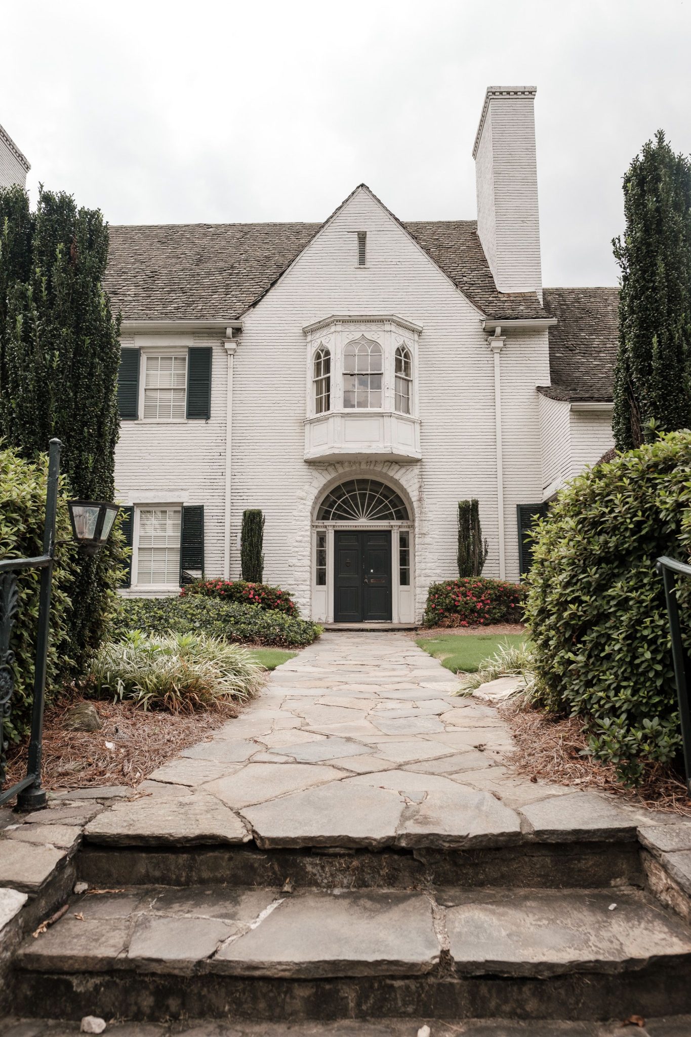 Elegant white brick house with arched doorway and landscaped garden.