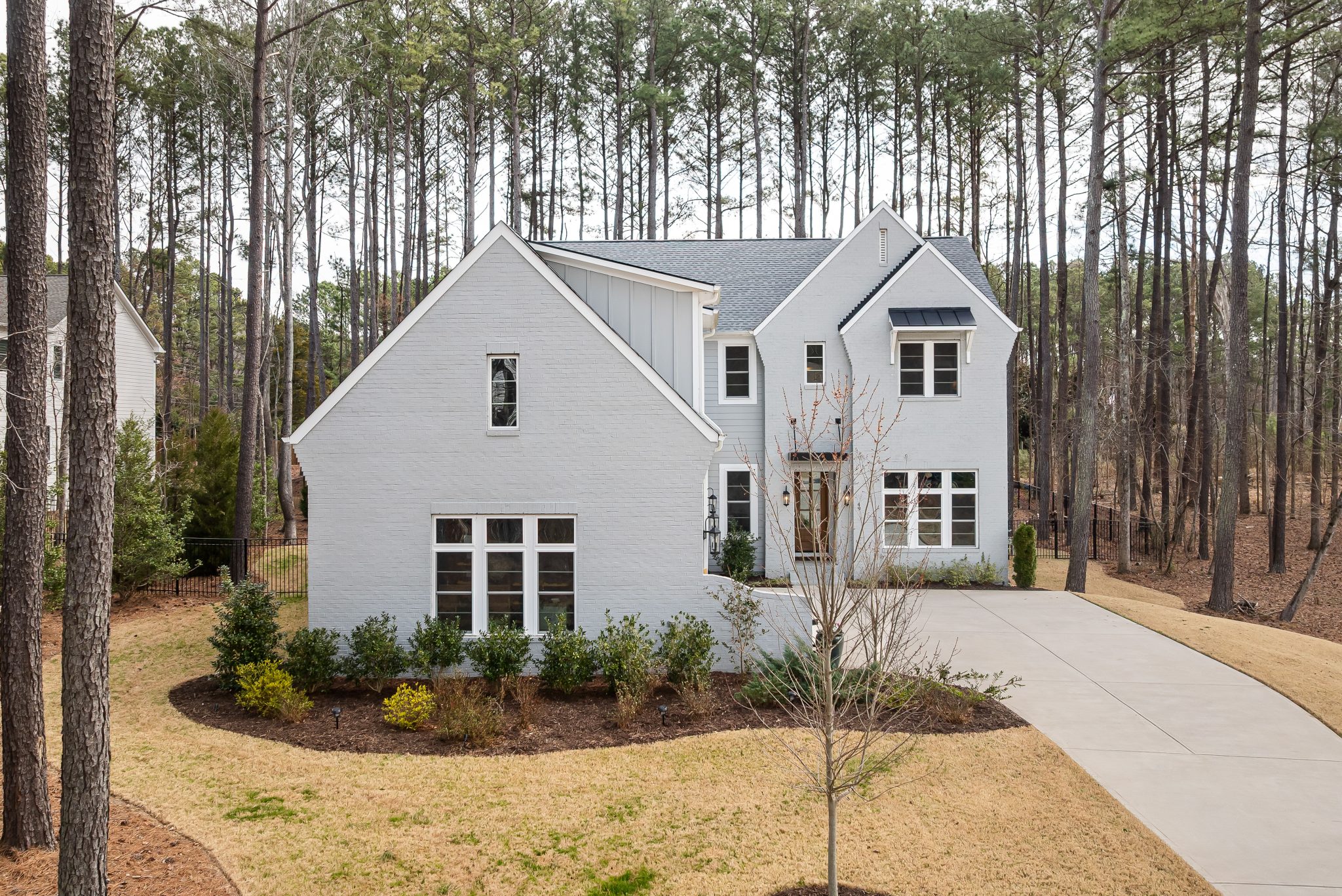 Elegant white two-story house amidst tall pine trees with a spacious driveway.