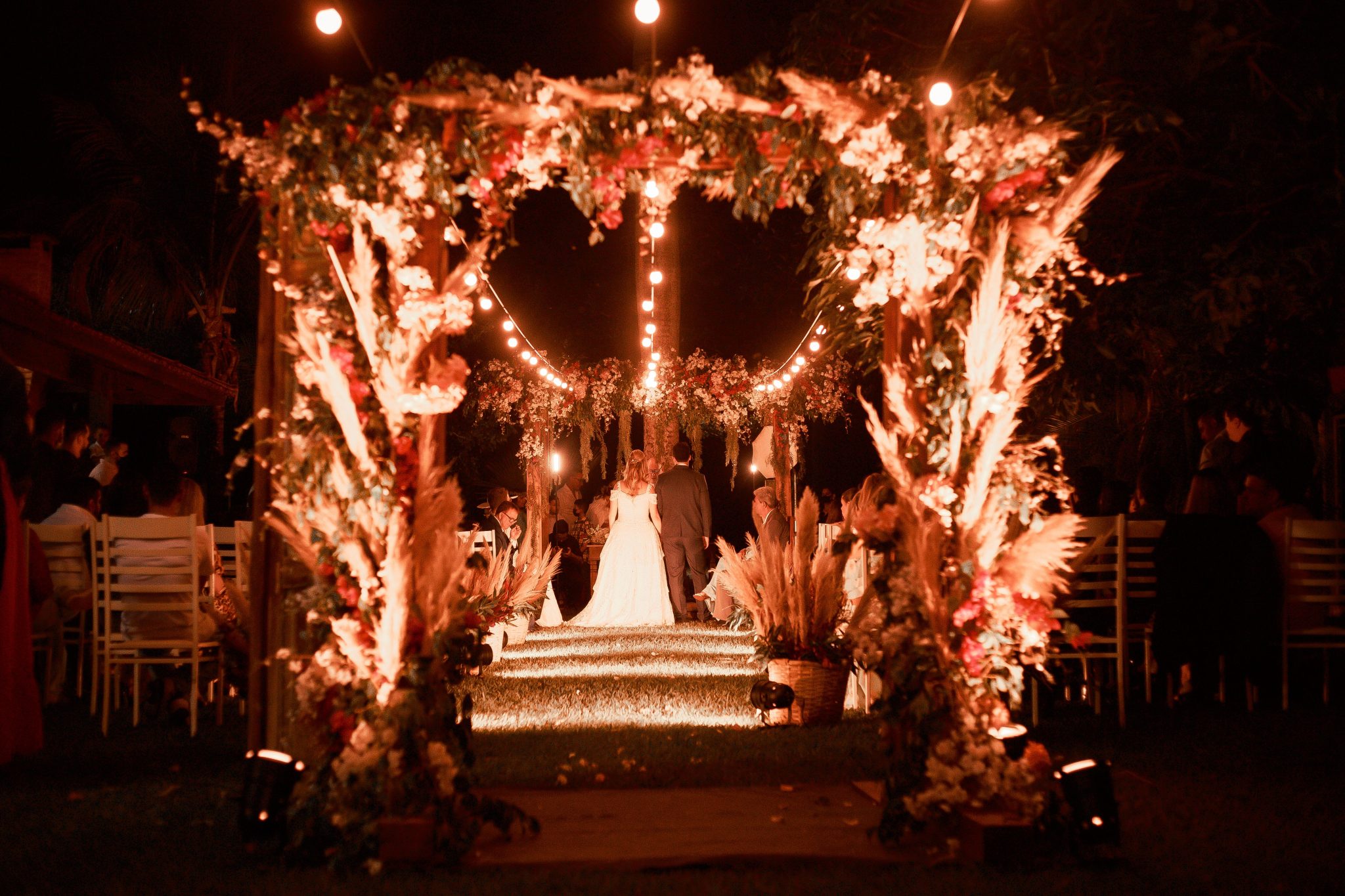Enchanting wedding ceremony under illuminated floral arch at night.