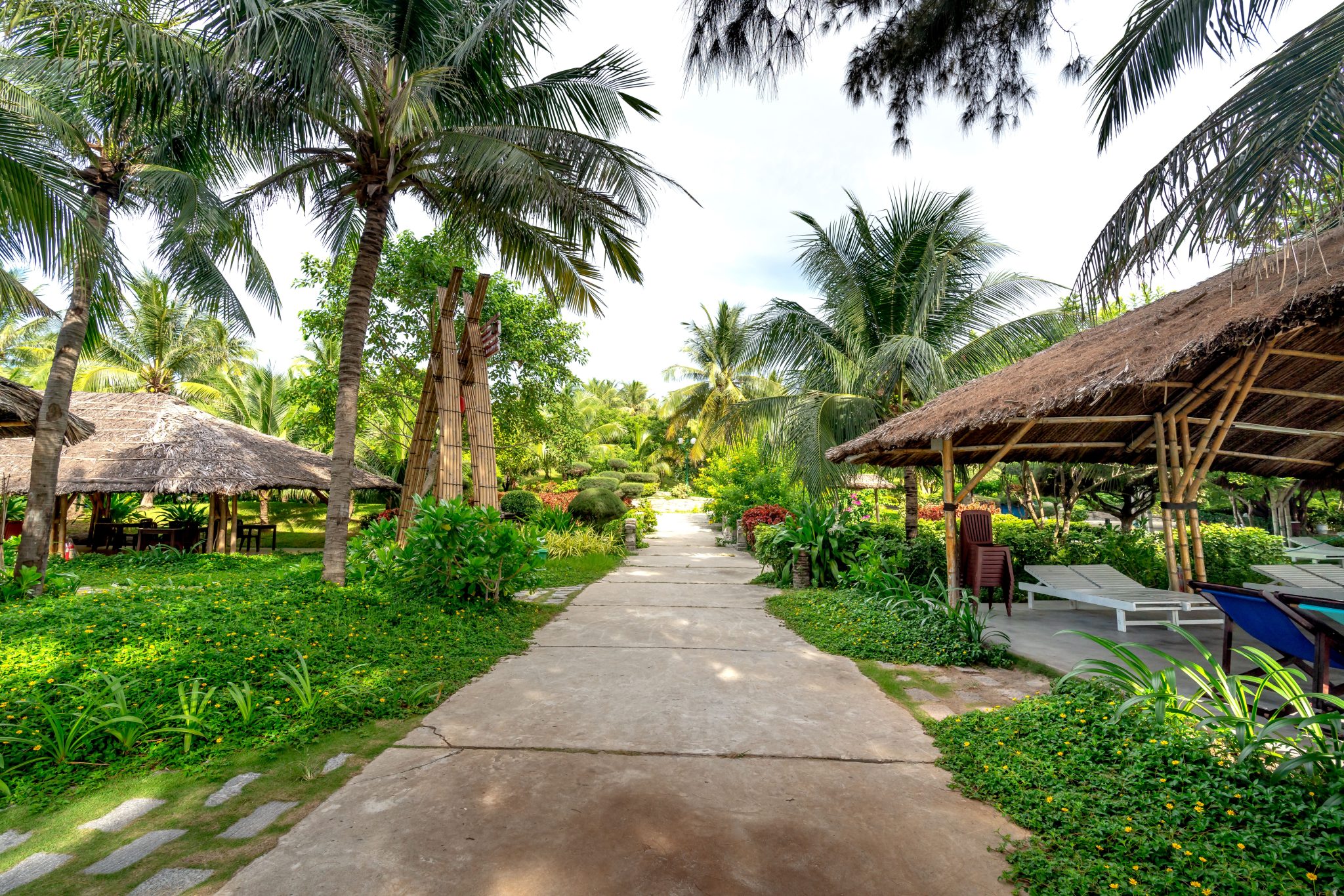 Idyllic tropical pathway with palm trees and thatched huts, perfect for a resort vacation setting.