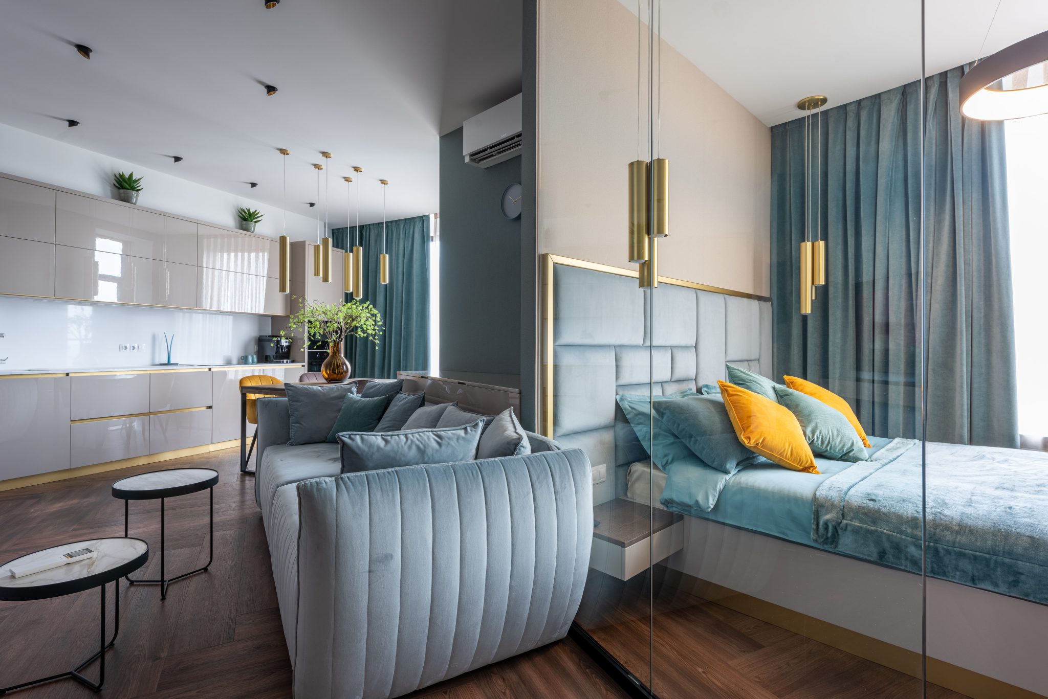 Interior of modern apartment with modern cabinets in kitchen and soft couch placed near bedroom with bed and glass wall