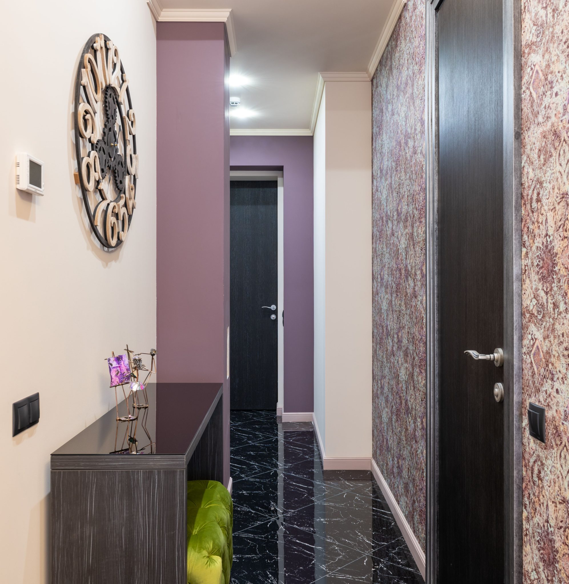 Interior of narrow corridor with decorations on wooden cupboard and entrance with black door in modern apartment with tiled floor