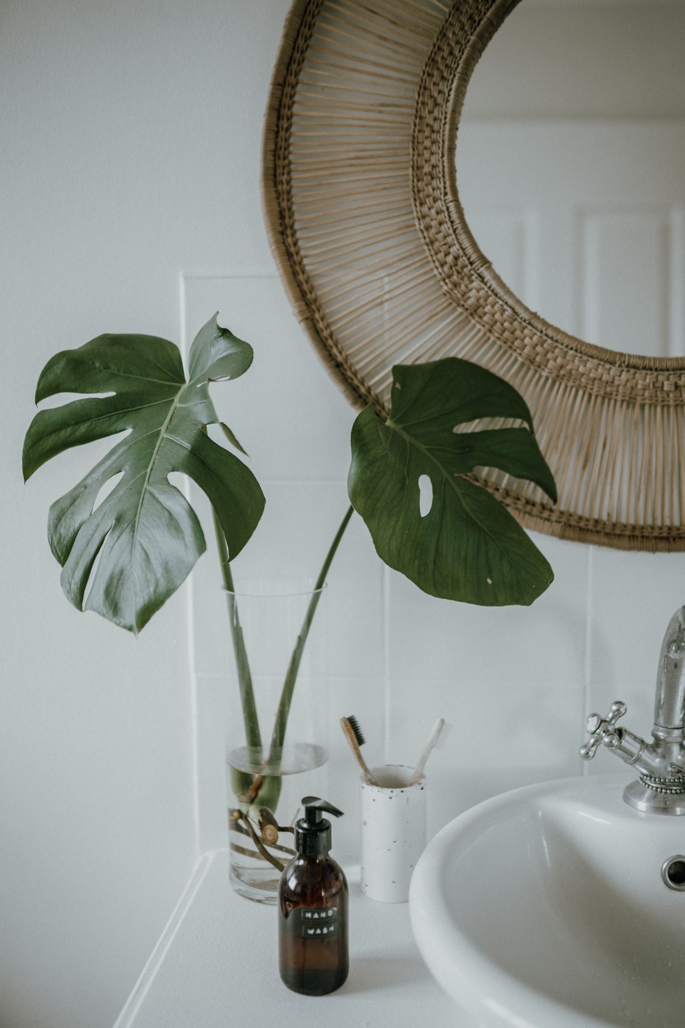 Modern bathroom with monstera plant and stylish wicker mirror, creating a fresh and elegant space.