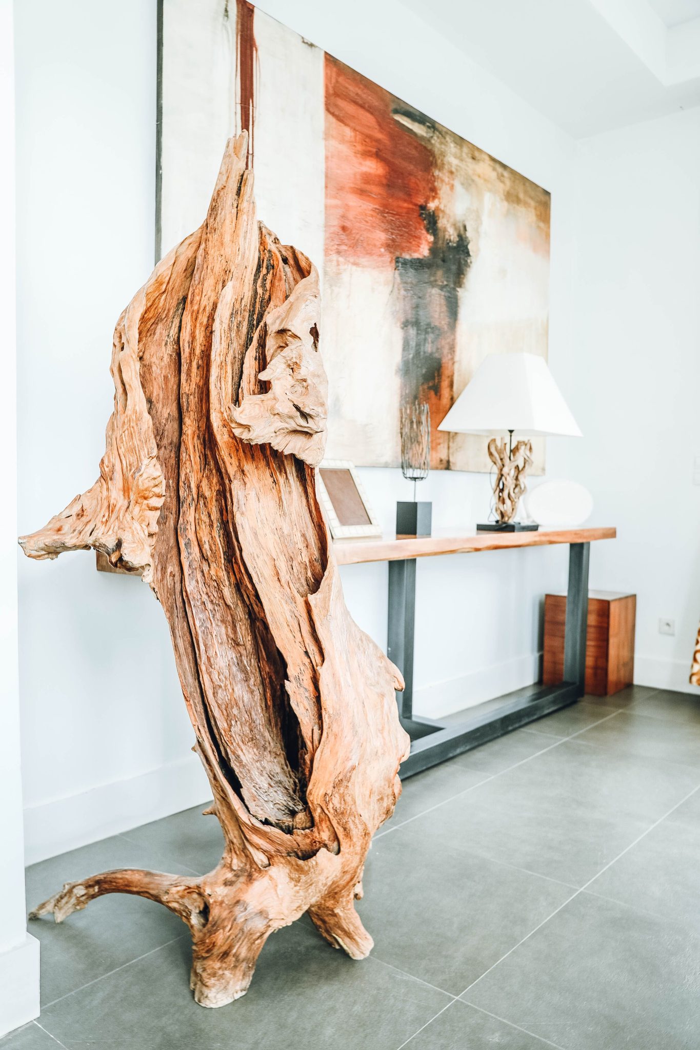 Modern interior design featuring a driftwood sculpture, wooden table, and abstract painting.