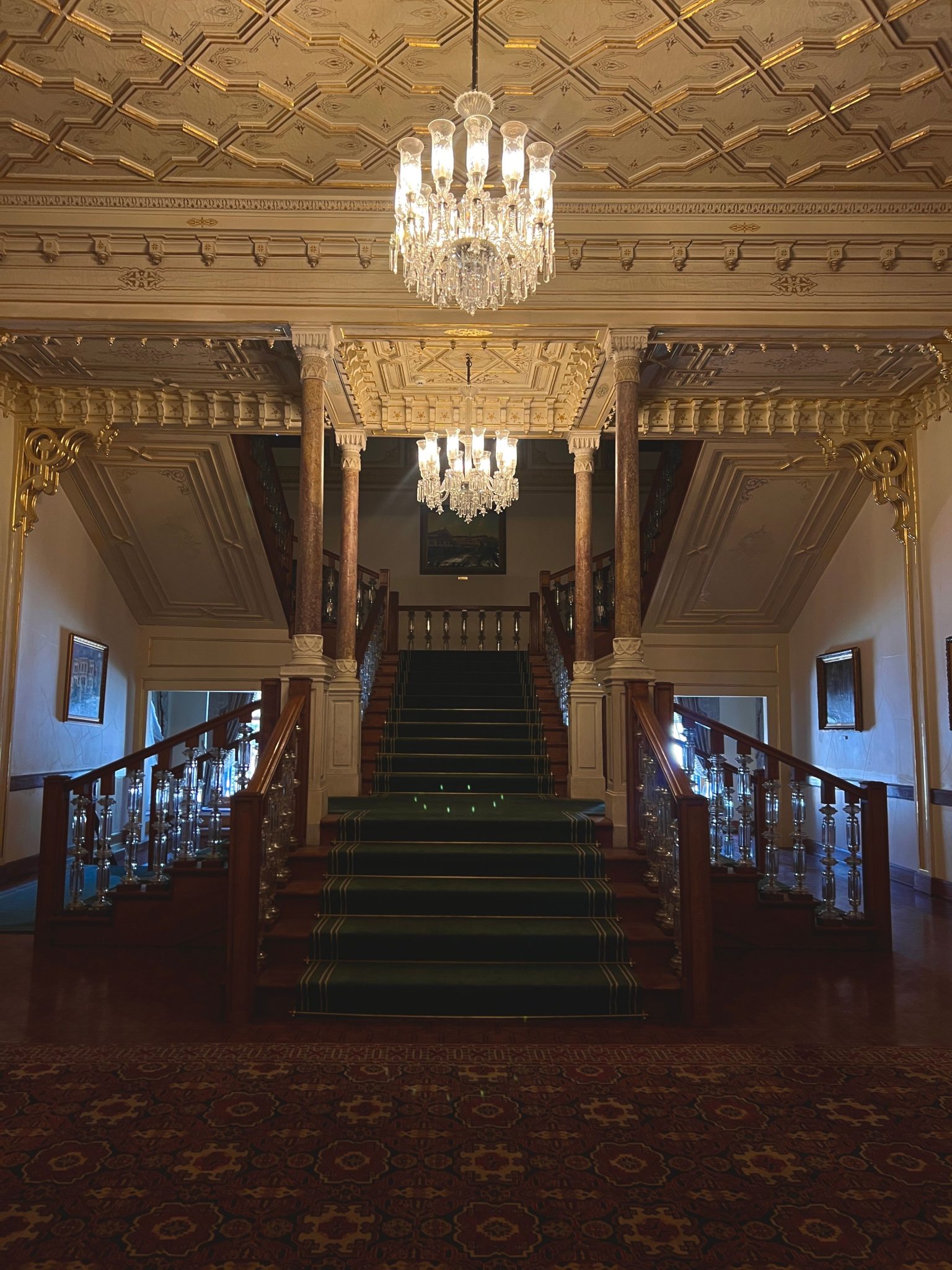 Opulent vintage staircase with chandeliers and rich decor.