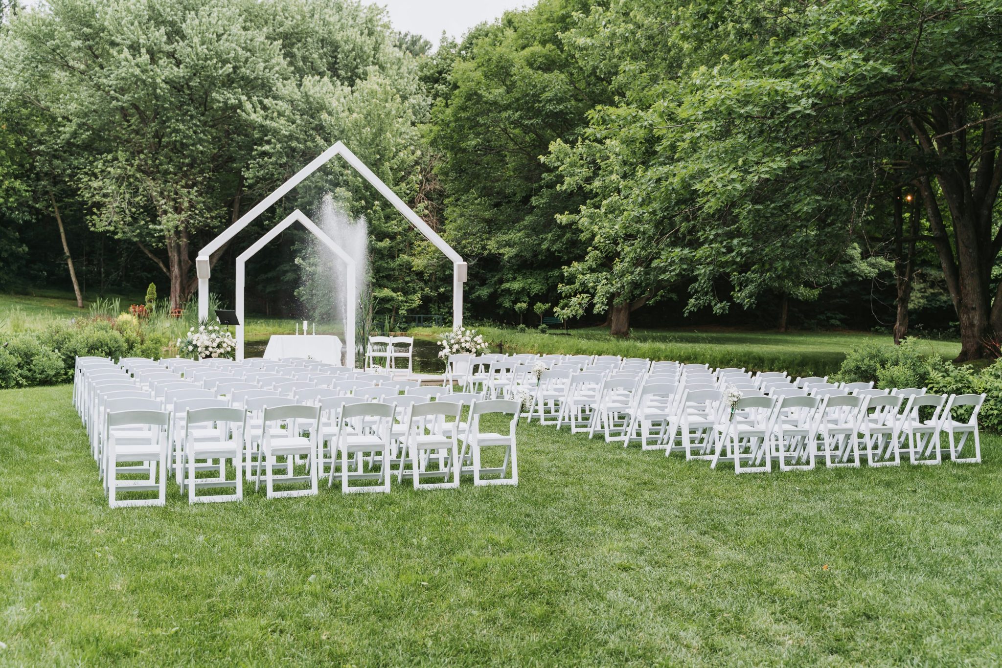 Outdoor wedding ceremony setup with white chairs and arch.