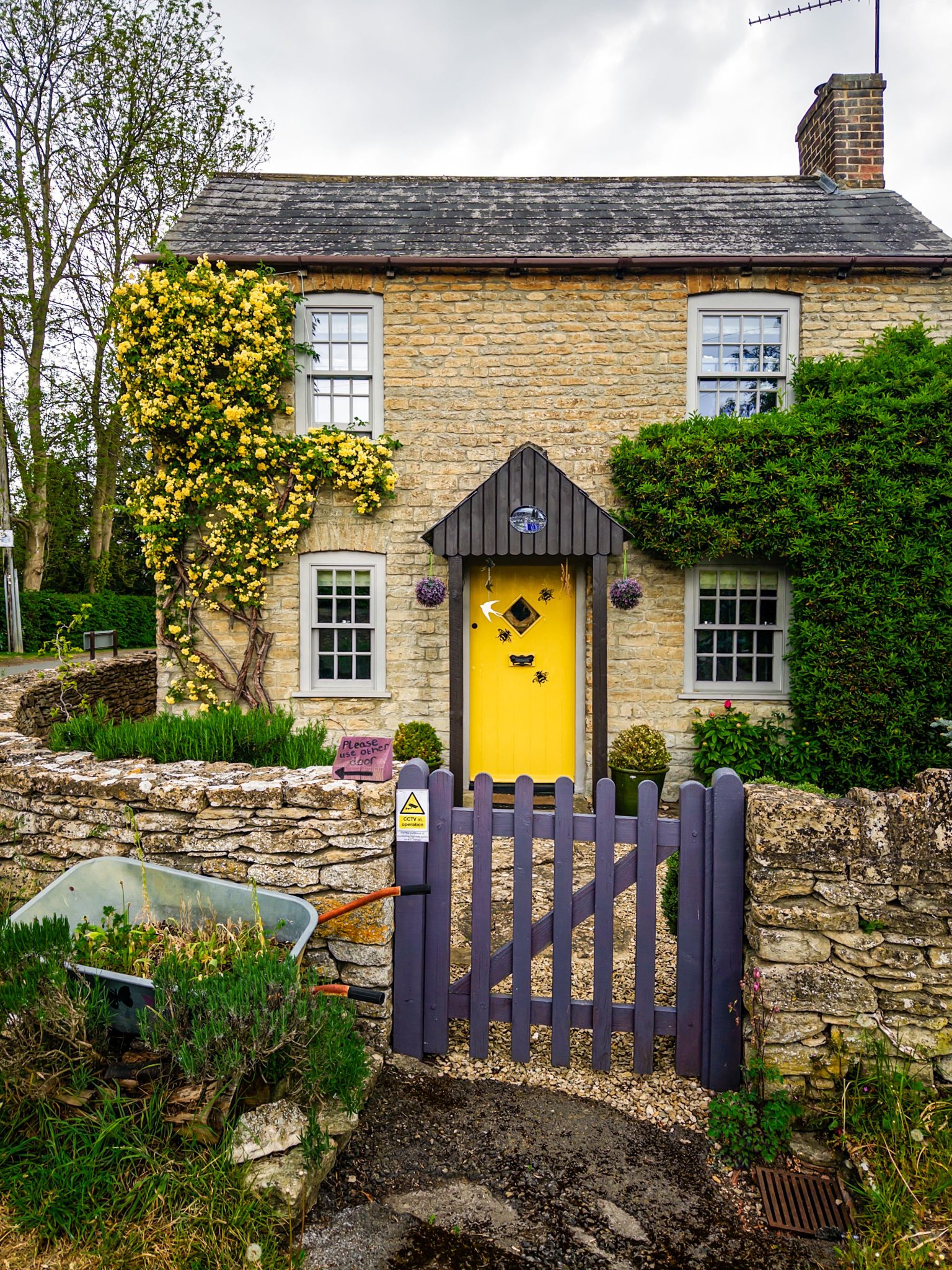 Picturesque stone cottage in Lea, England with vibrant yellow door and lush greenery.