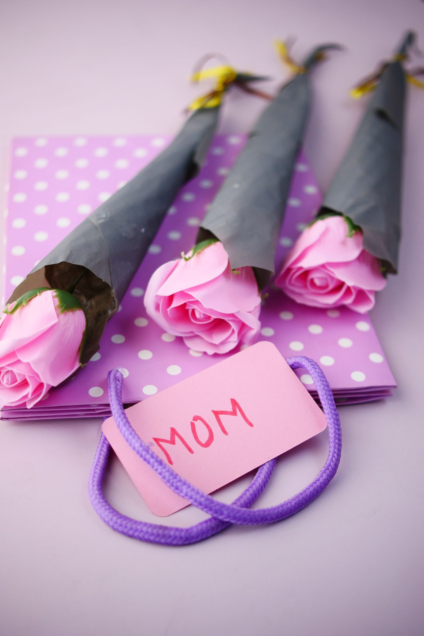 Pink roses and gift bag with 'Mom' label, perfect for Mother's Day celebrations.