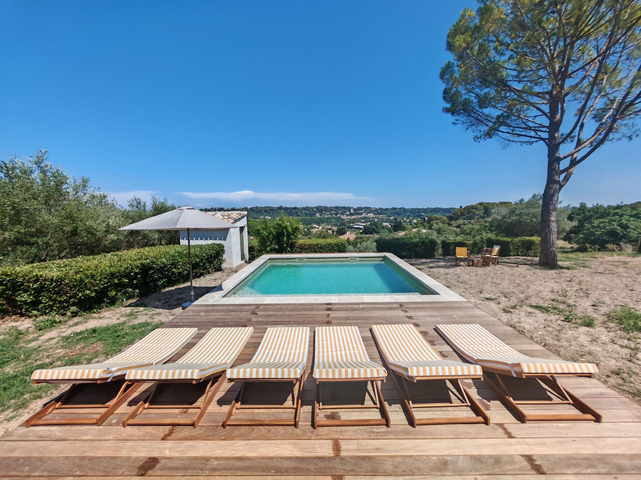 Relaxing outdoor scene with sun loungers by a private pool under a clear blue sky.