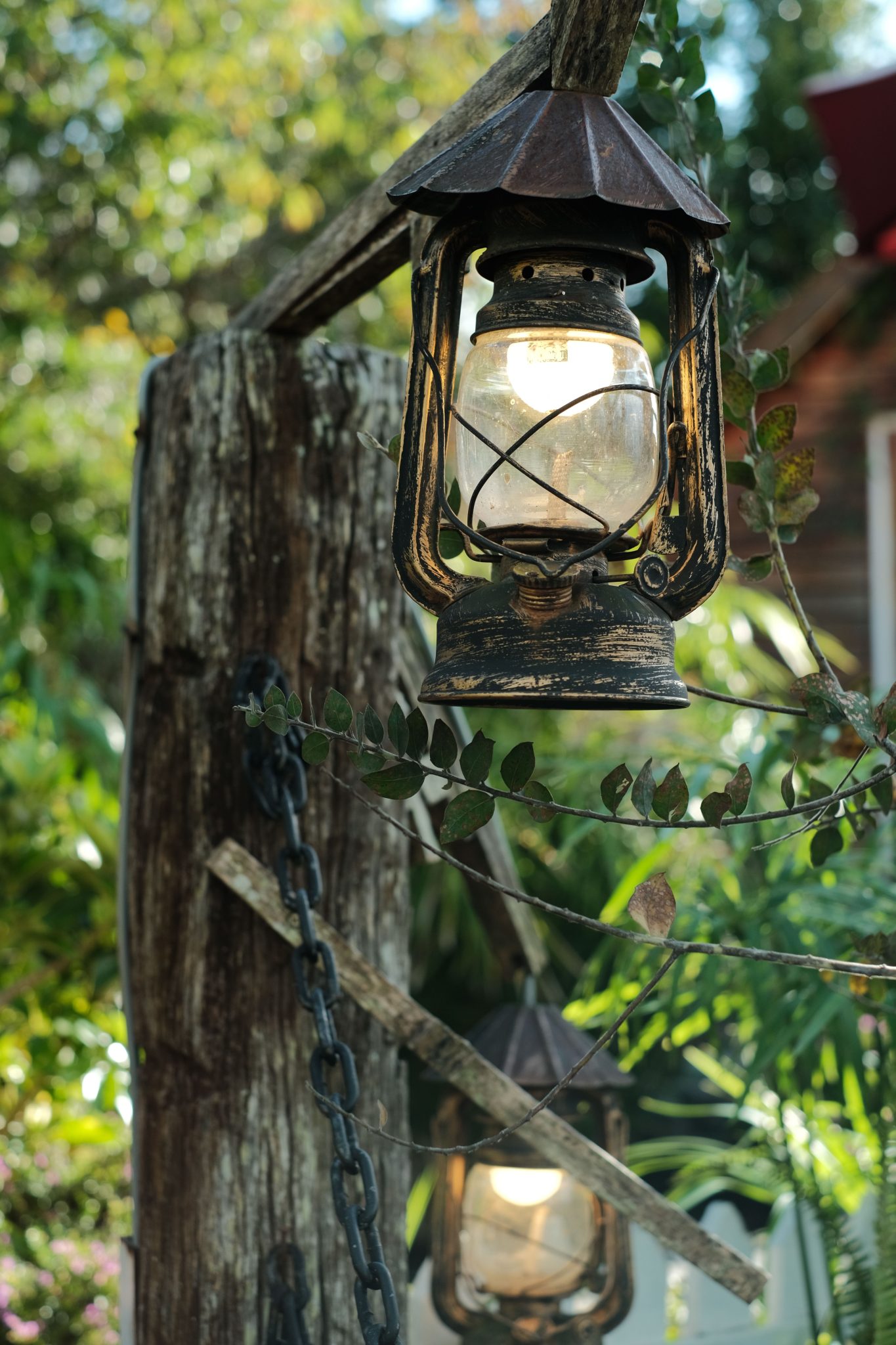 Rustic vintage lanterns hanging outdoors in a garden, surrounded by lush greenery and sunlight.