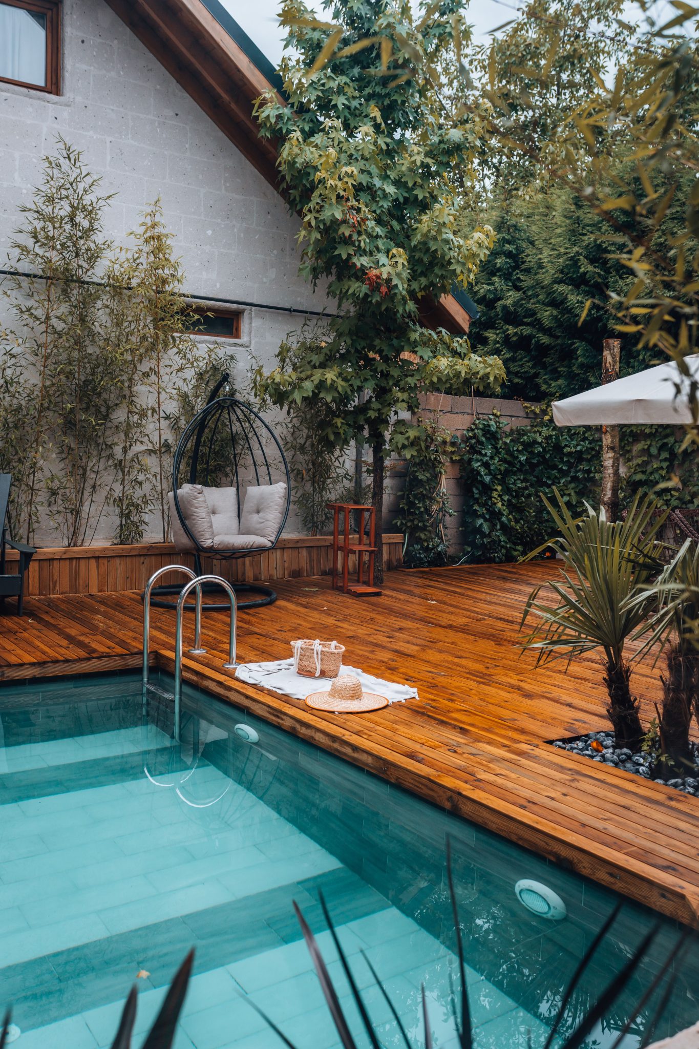 Serene backyard retreat with pool, wooden deck, and lush greenery.