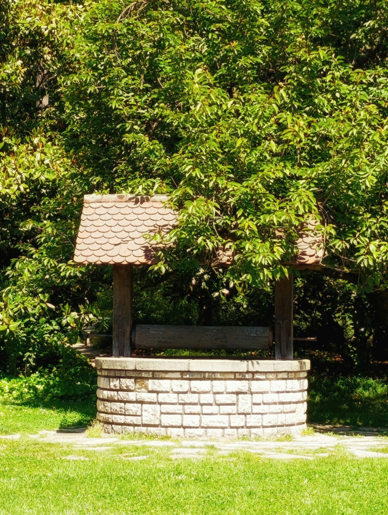 Stone wishing well with a shingled roof in greenery.