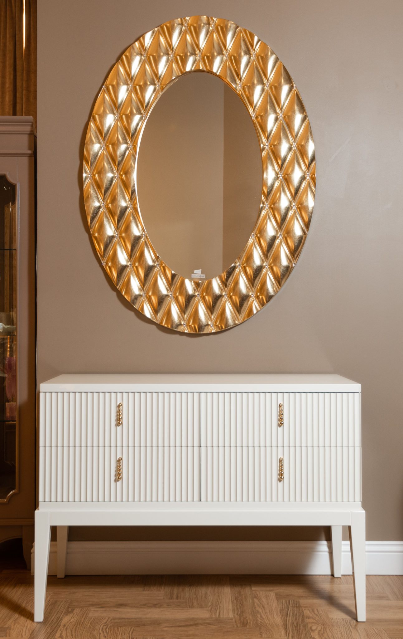 Stylish interior design featuring a gold ornate mirror above a sleek white cabinet against a neutral wall.