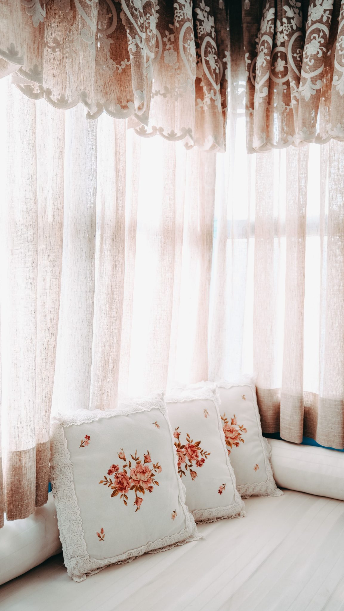 Sunlight pouring through floral patterned curtains and cozy cushions on a window seat.