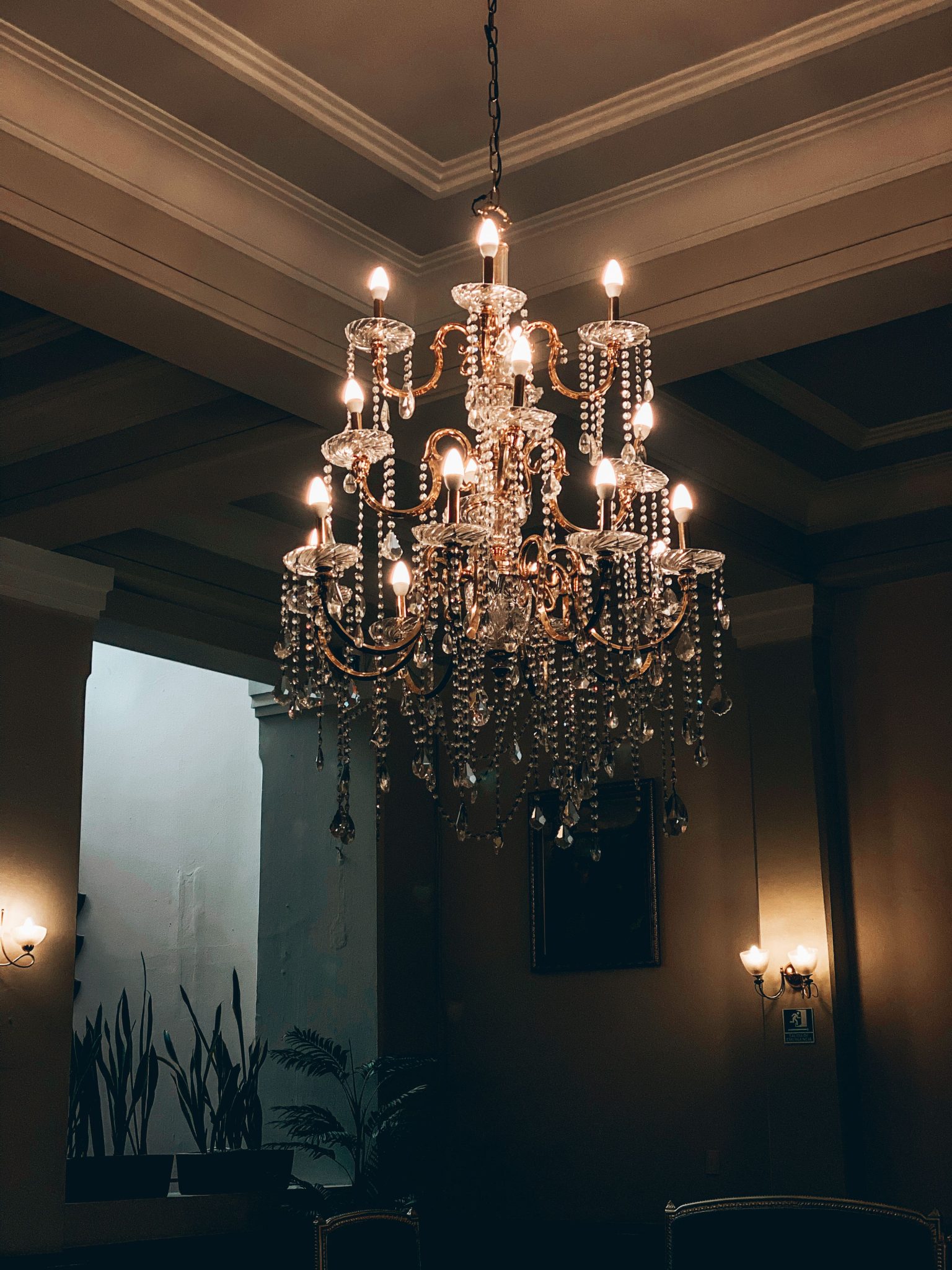 Vertical shot of a lit crystal chandelier in an ornate ceiling, evoking luxury.