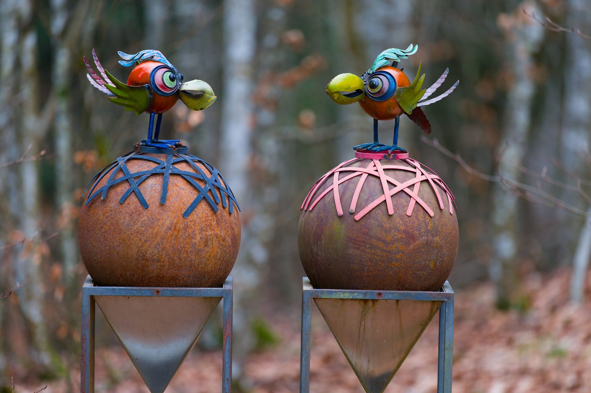 Vibrant metallic bird sculptures set against a forest backdrop in fall.