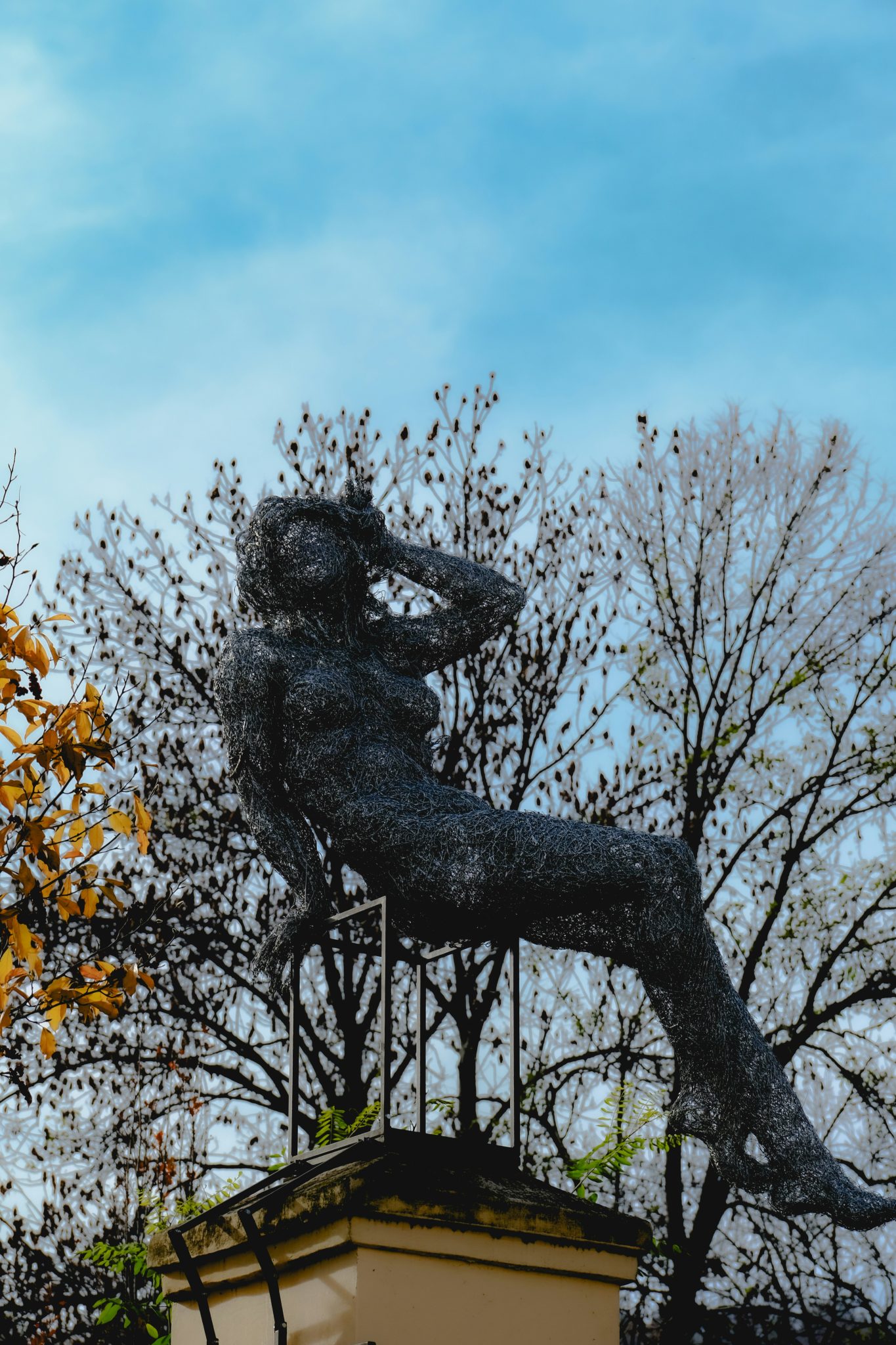 Wire sculpture of a reclining woman against trees