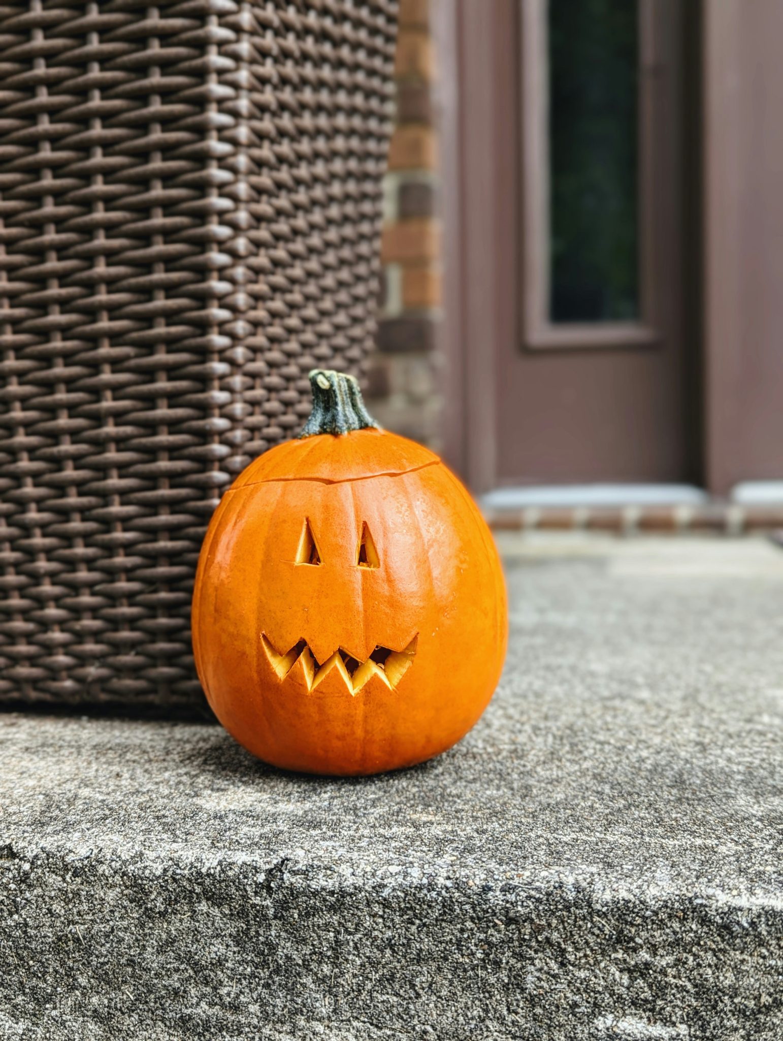 A carved pumpkin sitting on the steps of a house