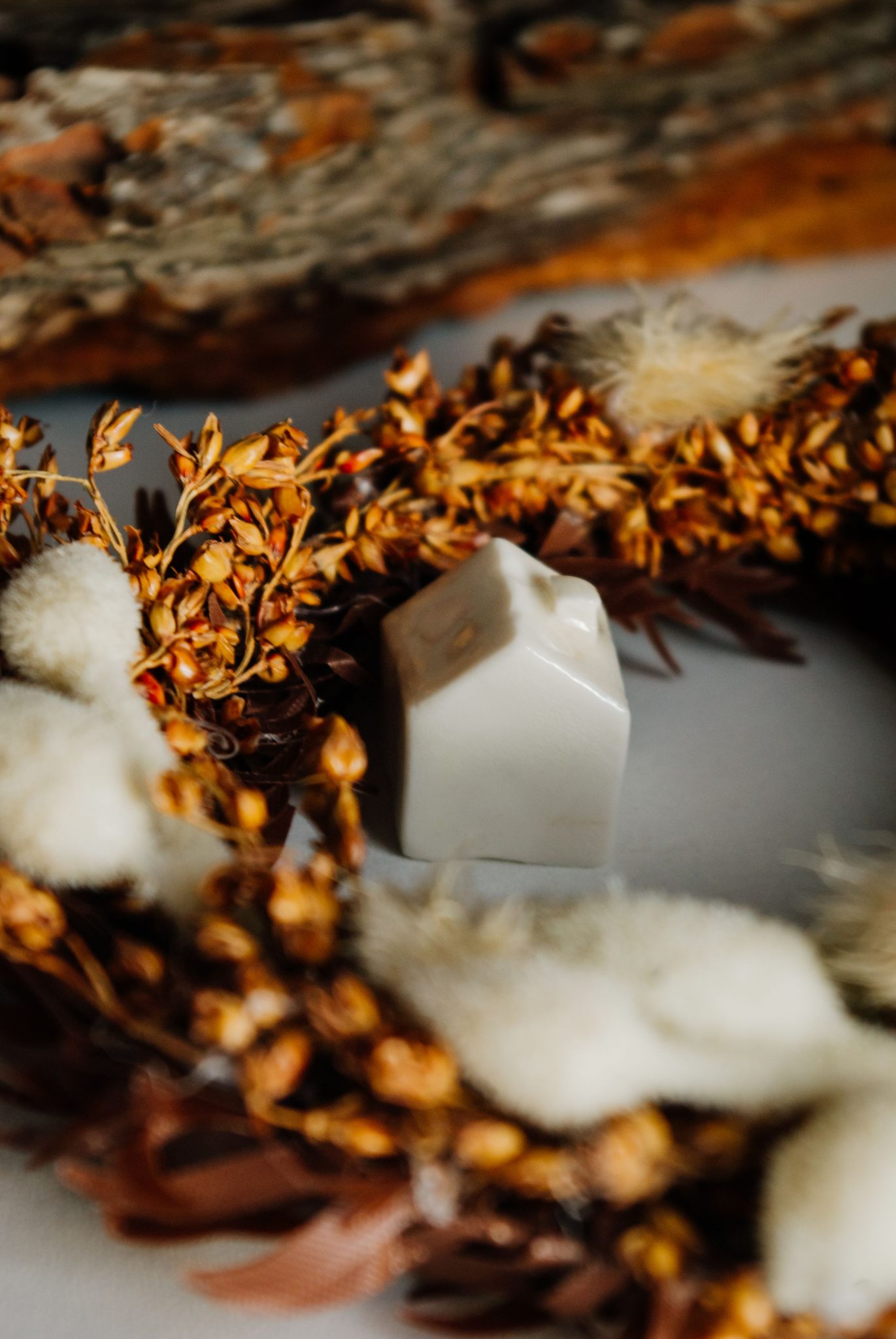 A ceramic house nestled in an autumn wreath, creates a cozy and rustic atmosphere.