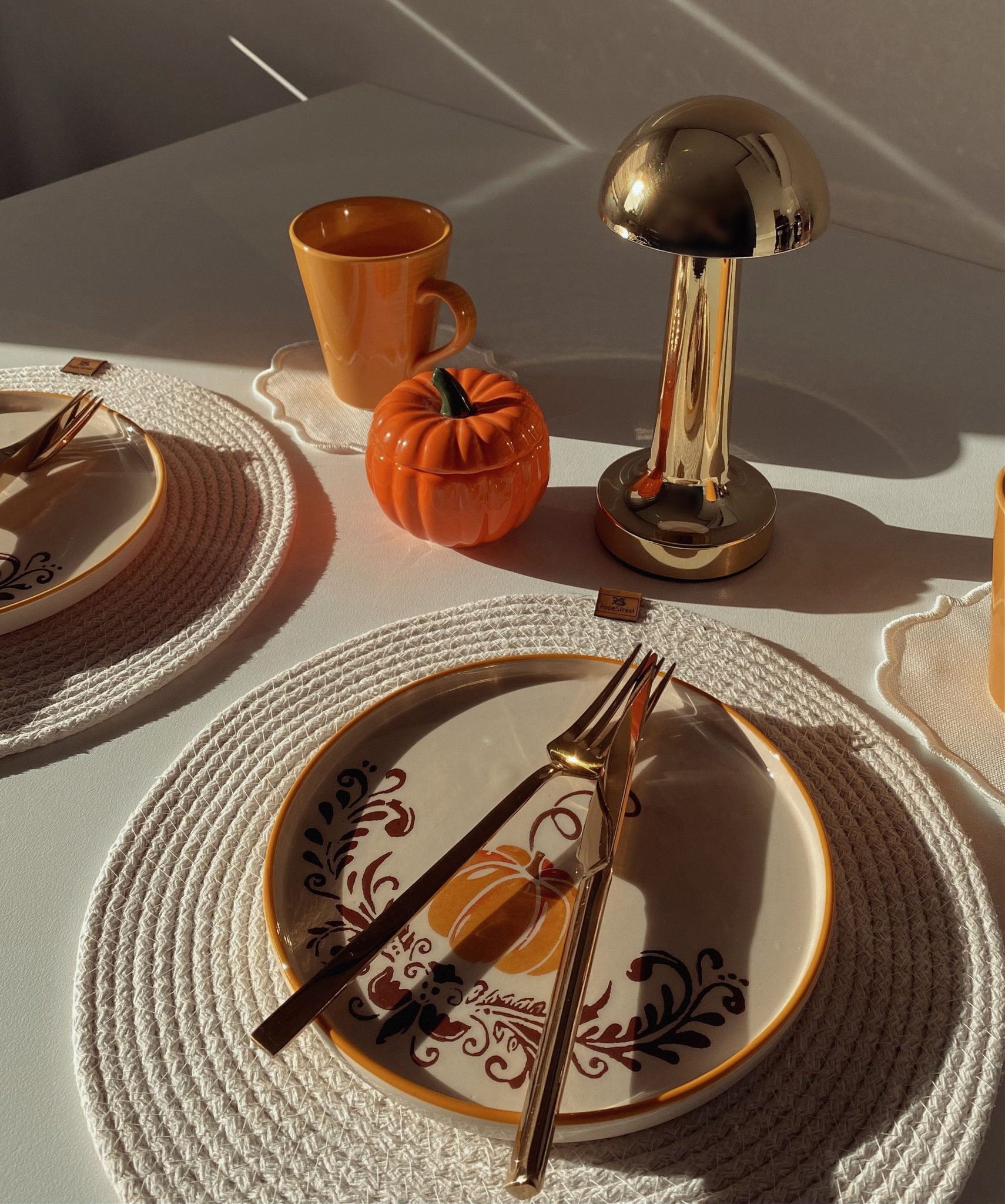 A cozy autumn table setup with pumpkin decor, golden cutlery, and warm lighting.