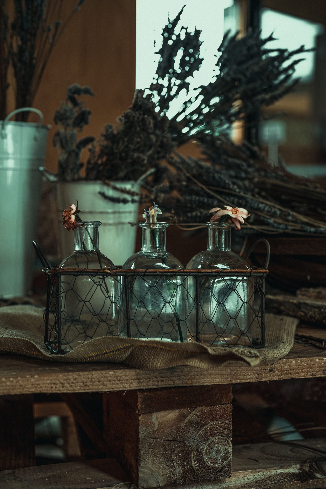 A cozy indoor setting with glass bottles on rustic wooden pallets adorned with dried flowers and herbs.
