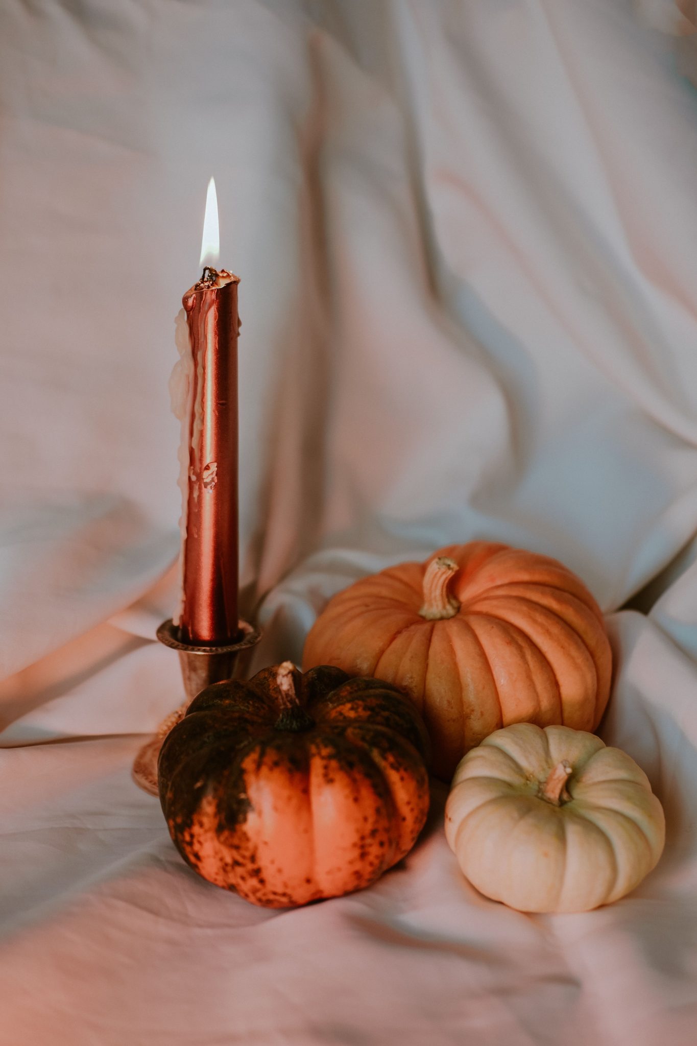 A cozy setup with three pumpkins and a candle, perfect for fall and Halloween decor.
