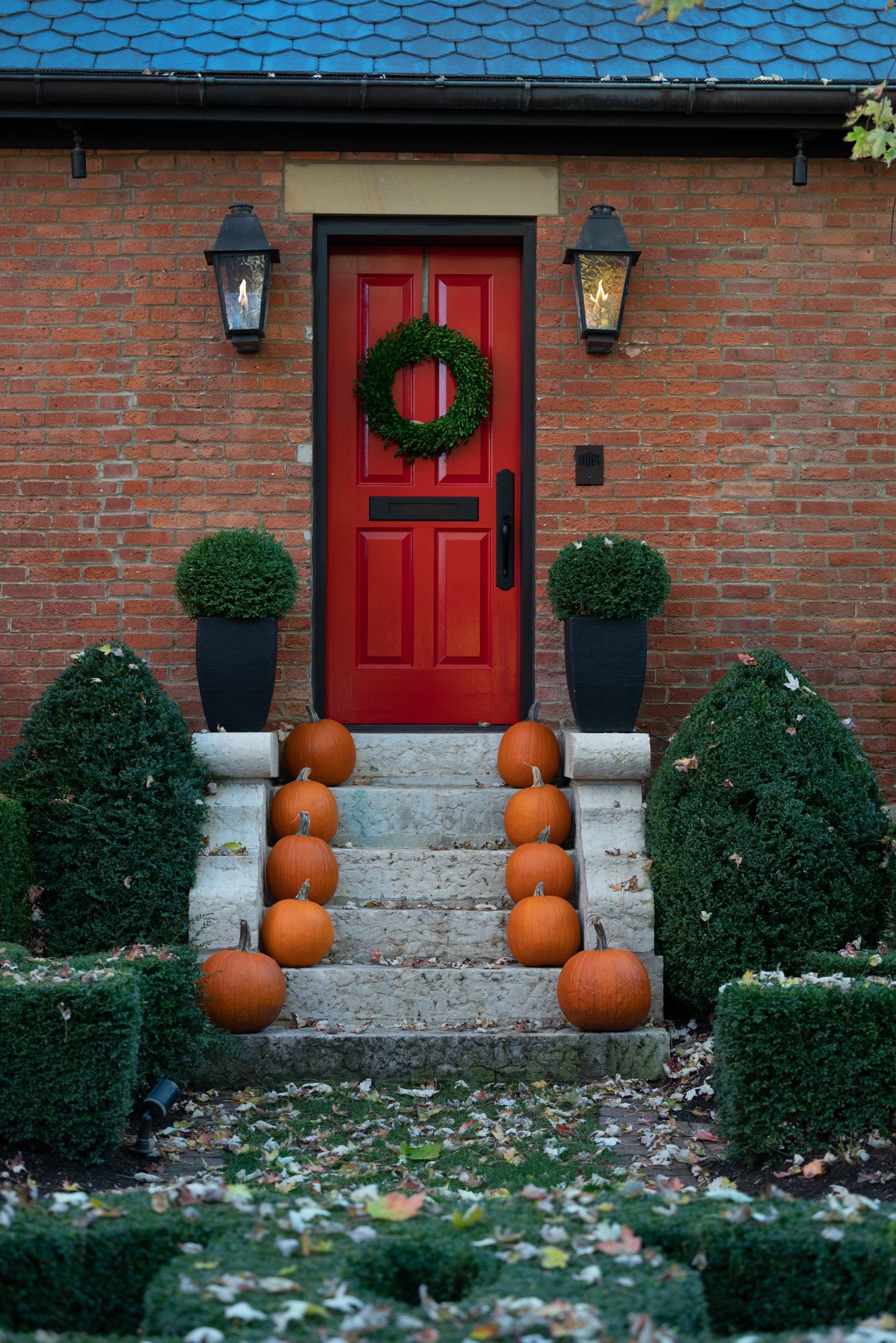 A festive entrance with pumpkins and a wreath on a red door, perfect for Halloween decoration.
