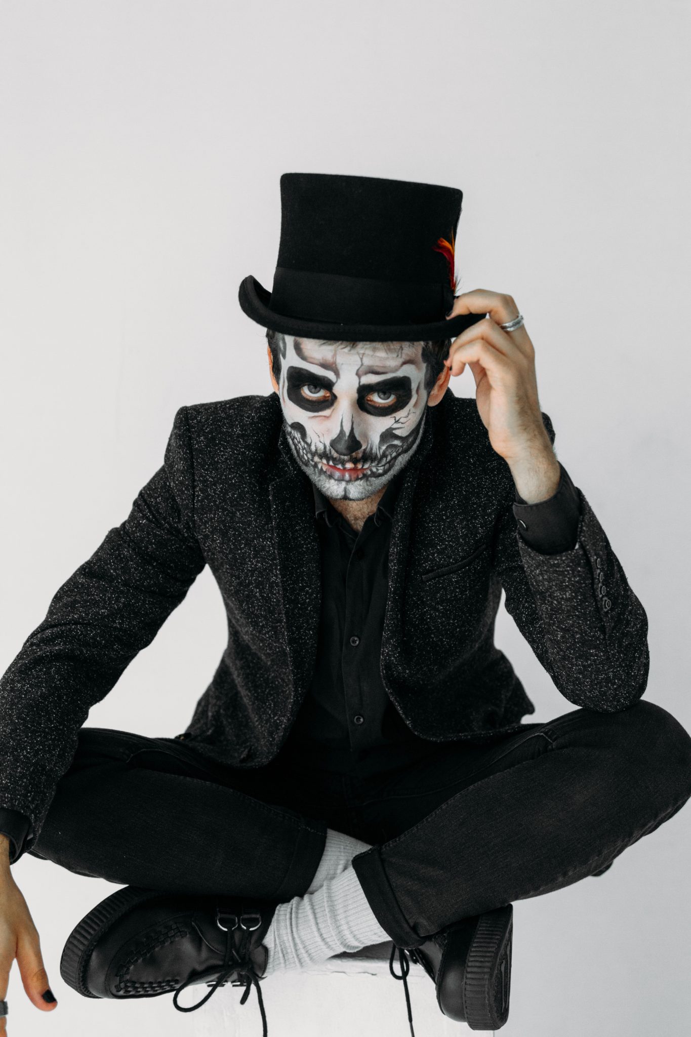A man in skull makeup and black suit posing indoors for Halloween.