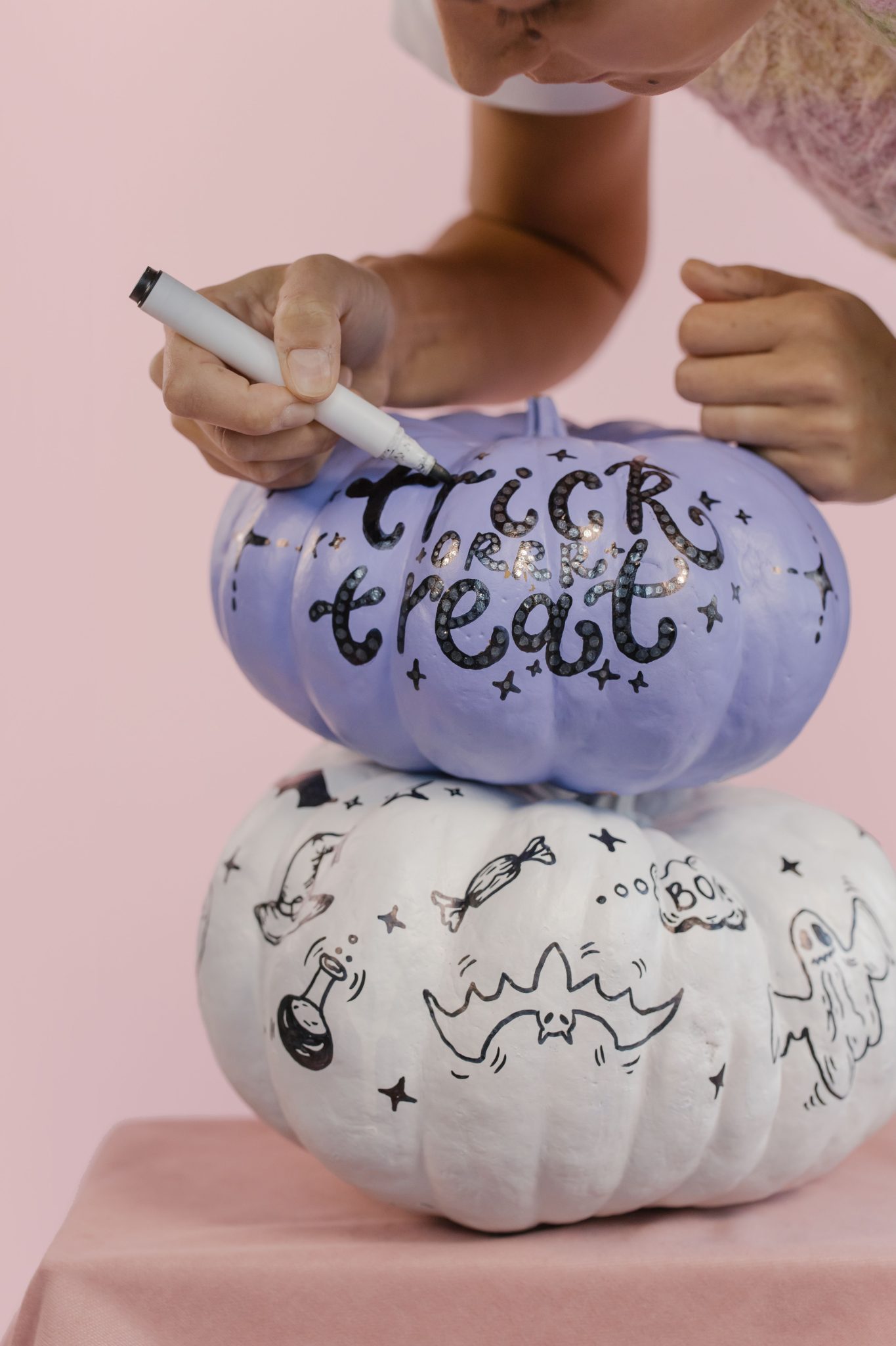 A person decorates stacked pumpkins with Halloween-themed designs and text.