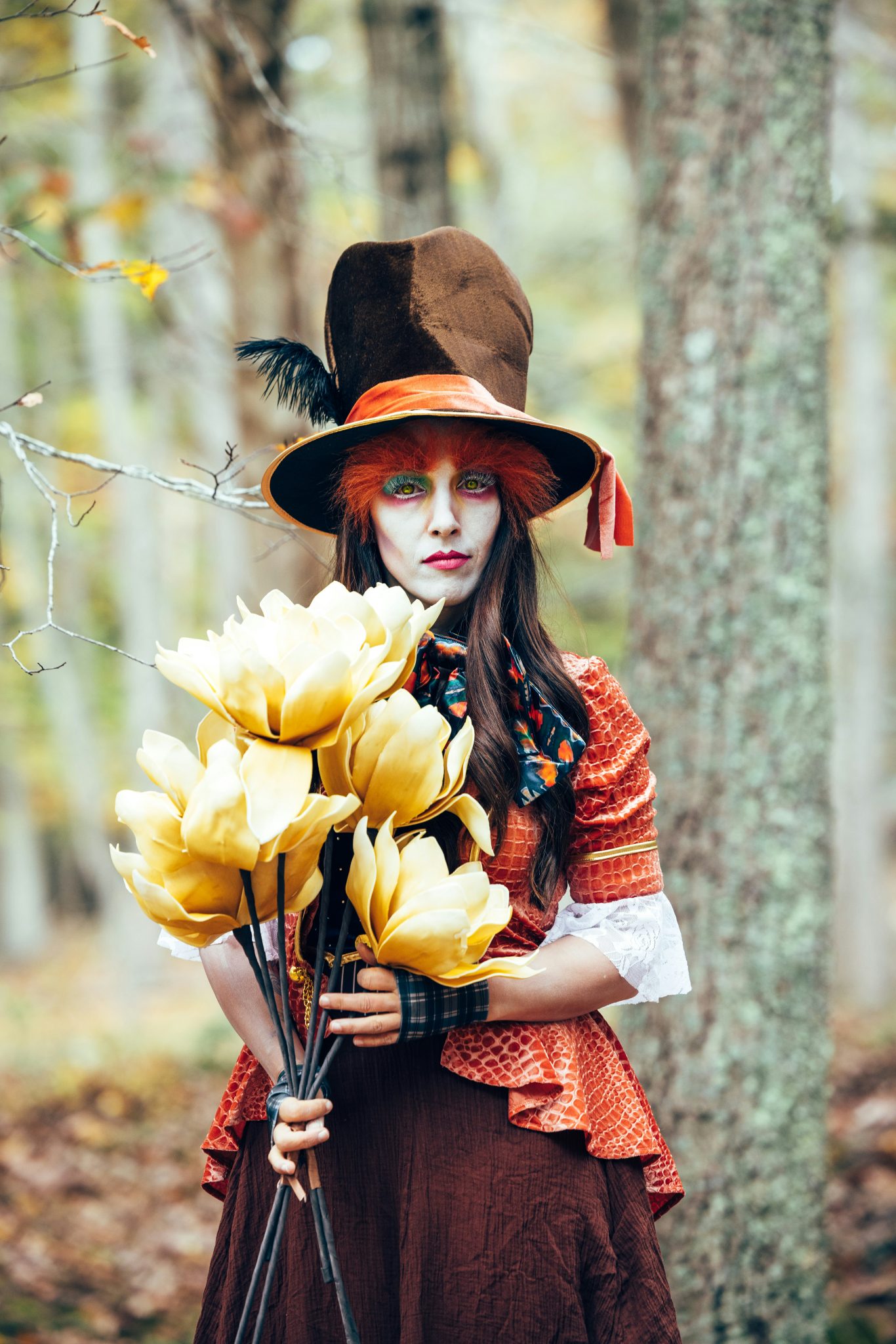 A person in a mad hatter costume holds yellow flowers