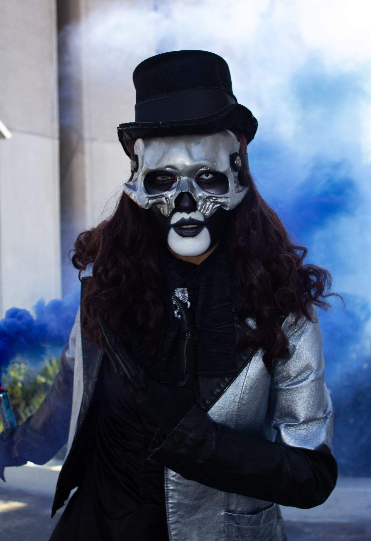A person in a striking skull mask and top hat amid blue smoke.