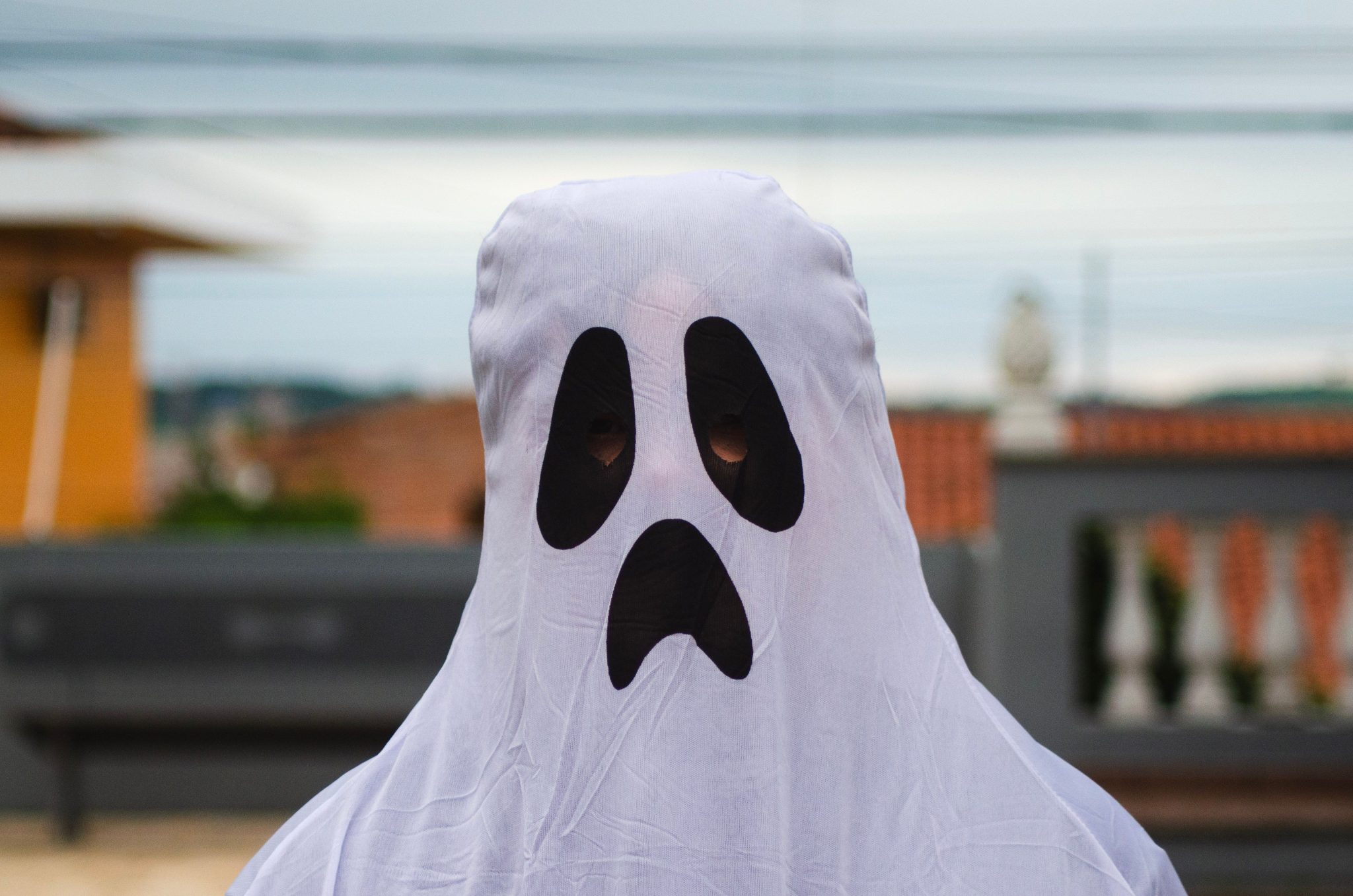 A person wearing a ghost costume with a spooky face stands outdoors.