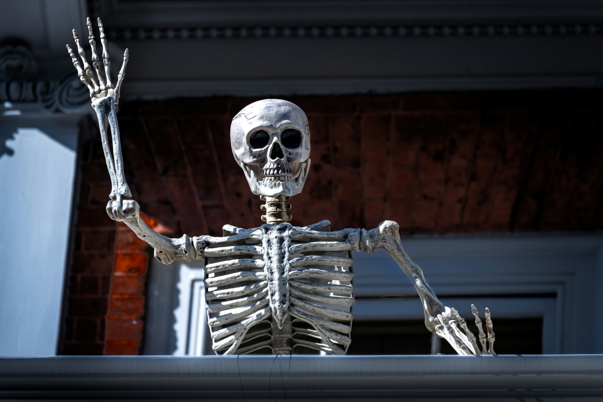 A playful skeleton decoration waving in front of a historic brick mansion during Halloween in Charleston, South Carolina.