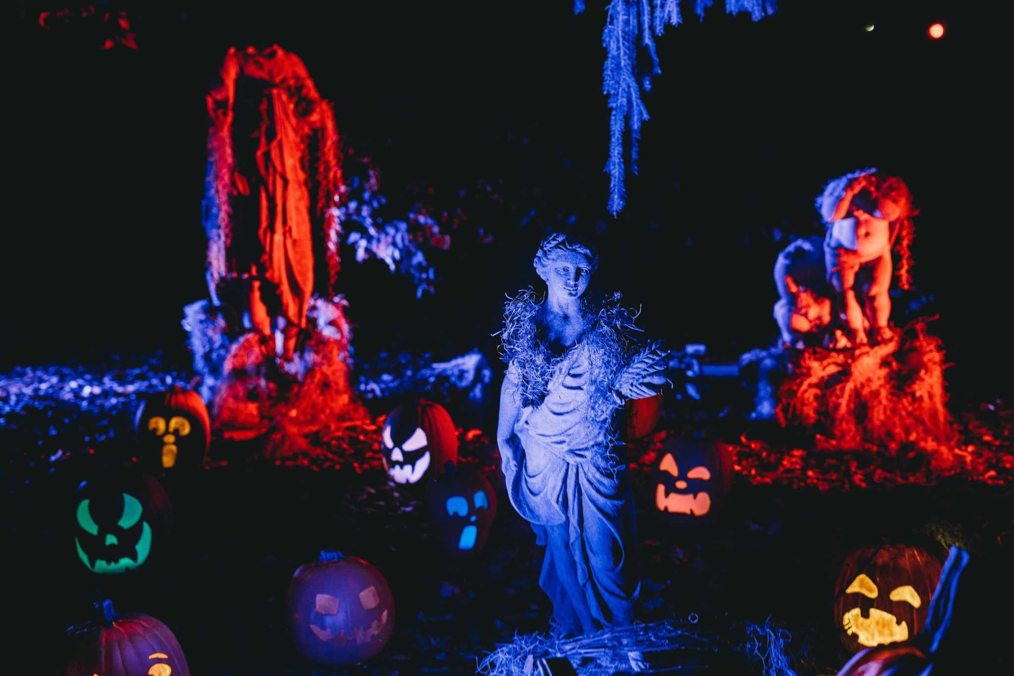 A spooky Halloween display featuring illuminated pumpkins and eerie sculptures at night.