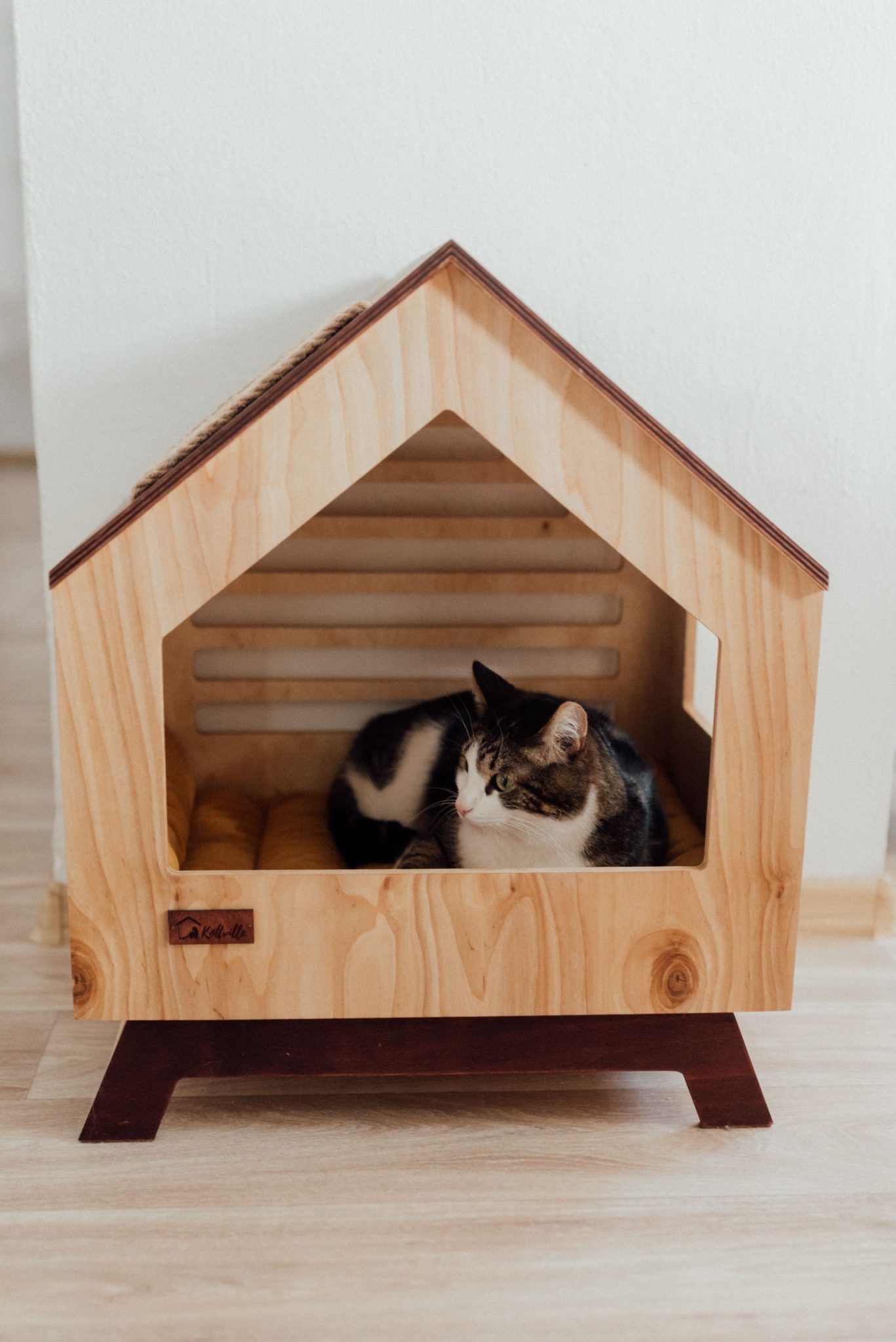 A tabby cat lounging inside a charming wooden pet house, perfect for indoor settings.