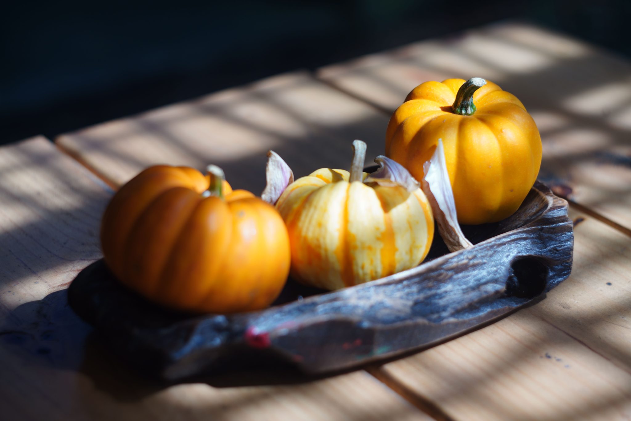 A trio of small decorative pumpkins on a rustic wooden tray with natural lighting.