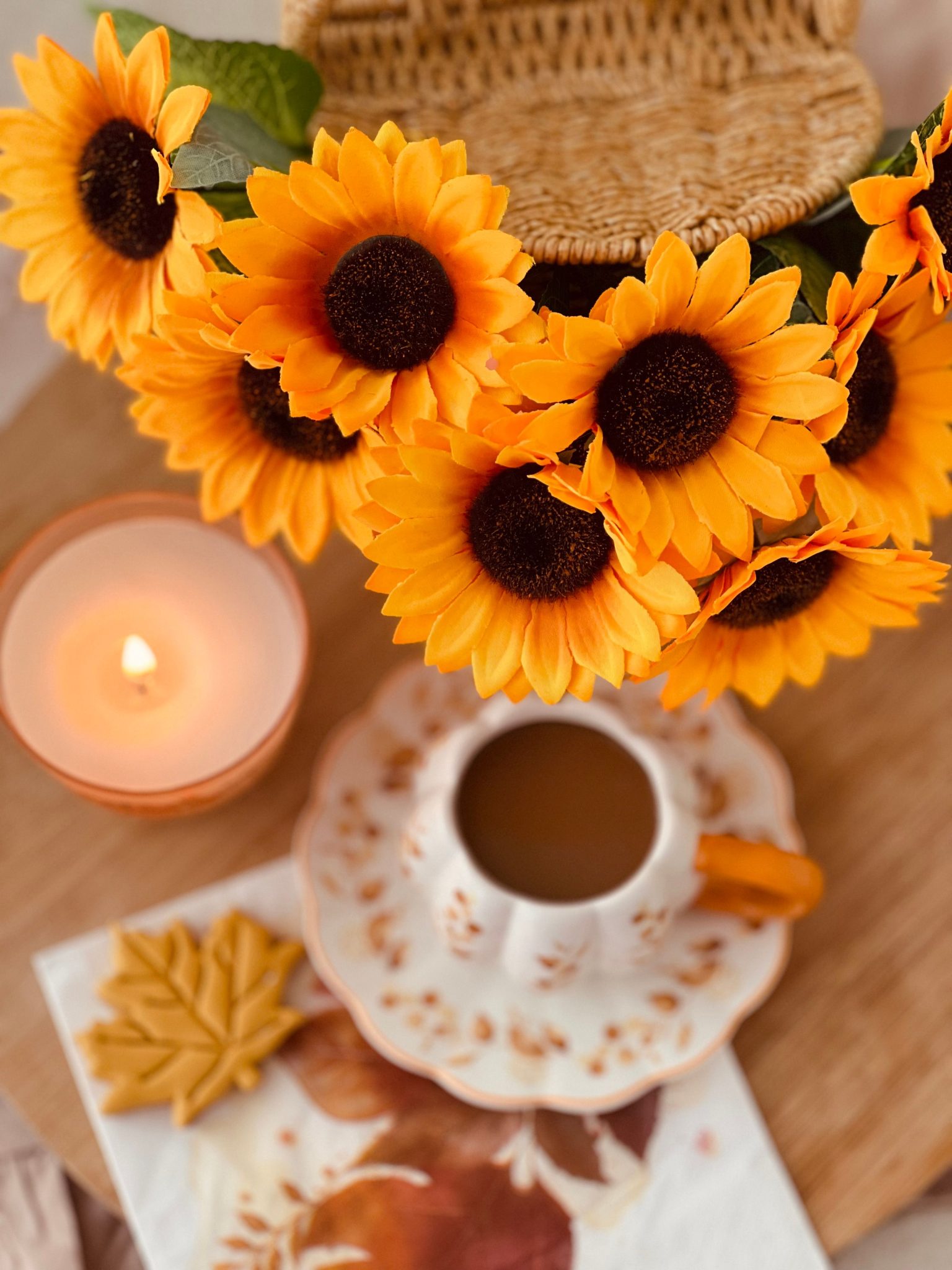 A warm autumn setting with sunflowers, coffee, candle, and leaves.