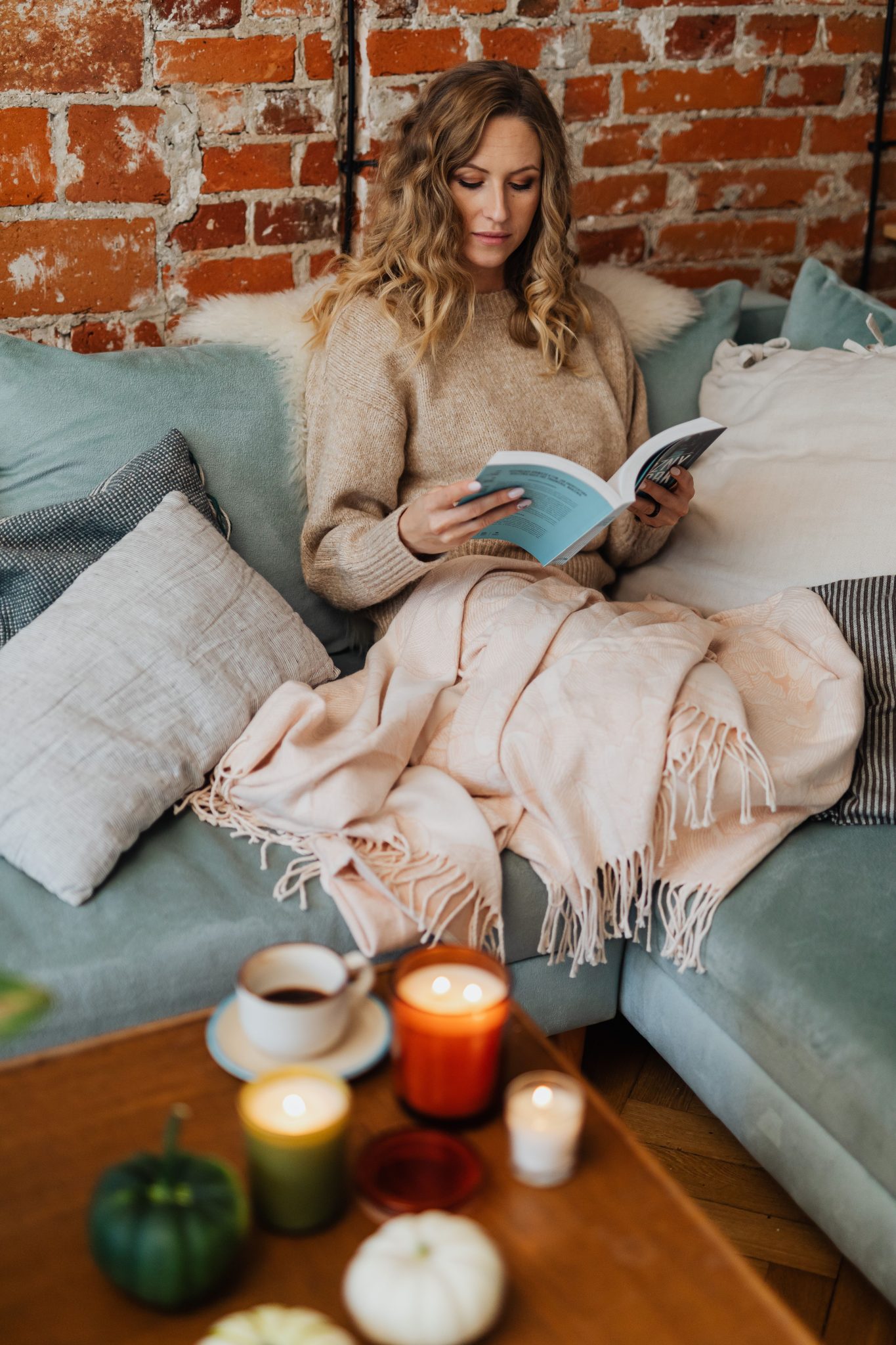 A woman enjoys a quiet reading moment on a sofa with candles creating a warm atmosphere.