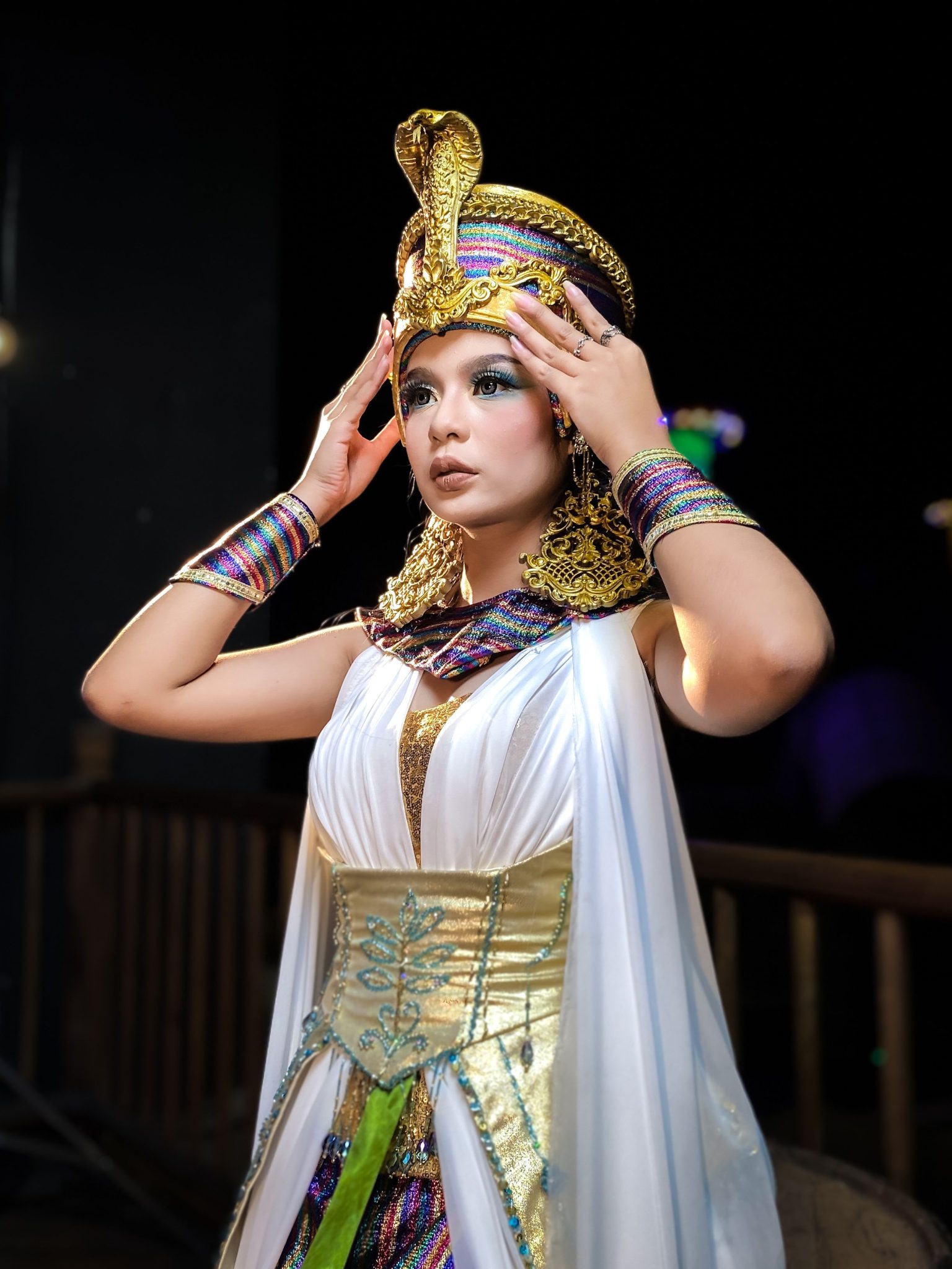 A woman in a detailed Cleopatra-inspired costume poses elegantly indoors.