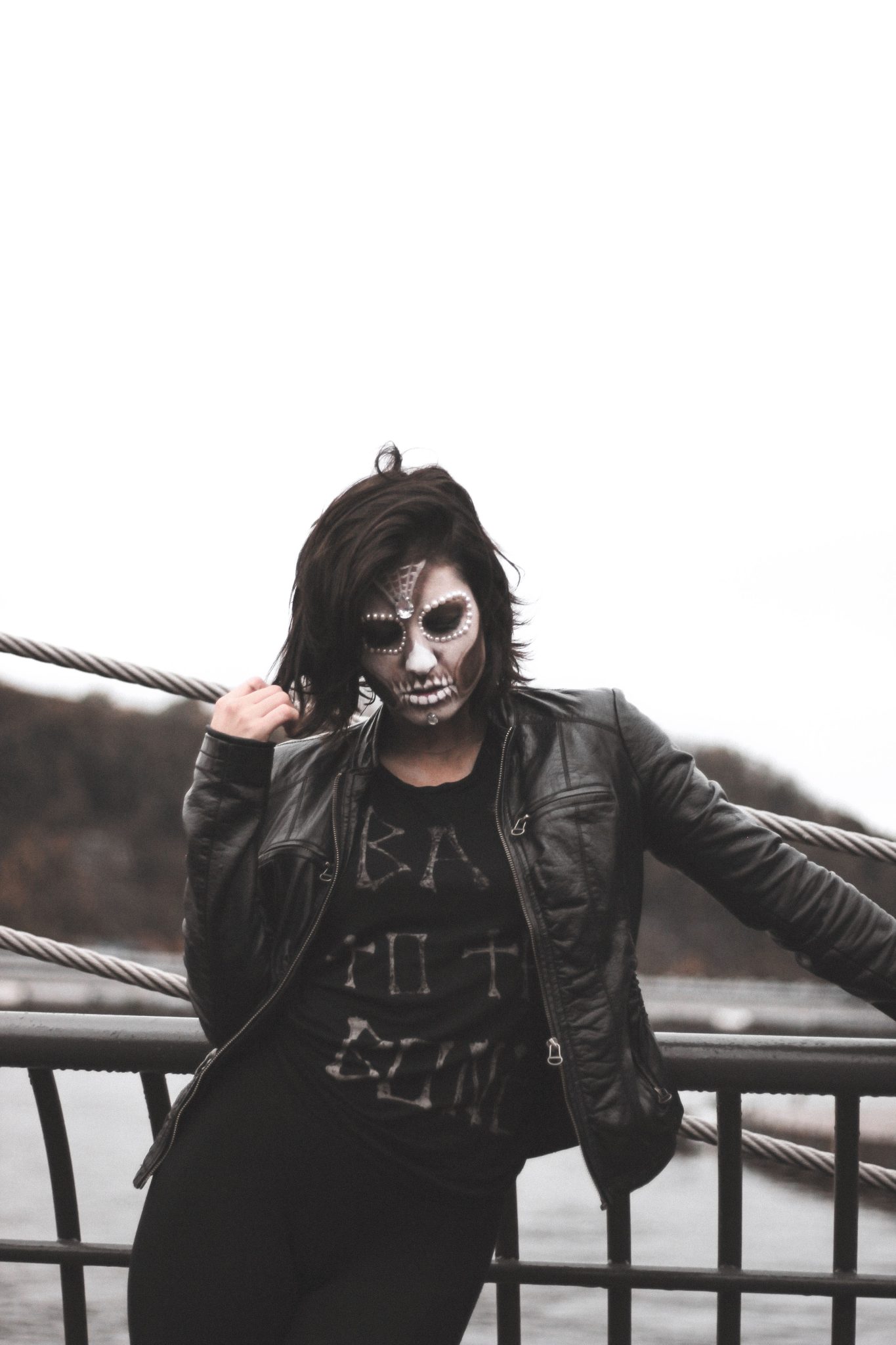 A woman with gothic face paint posed outdoors in a black leather jacket, adding mystery and allure.