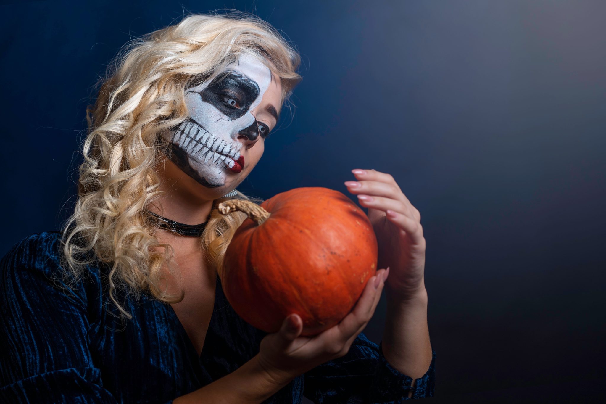 A woman with skull face paint holding a pumpkin, capturing the eerie essence of Halloween.