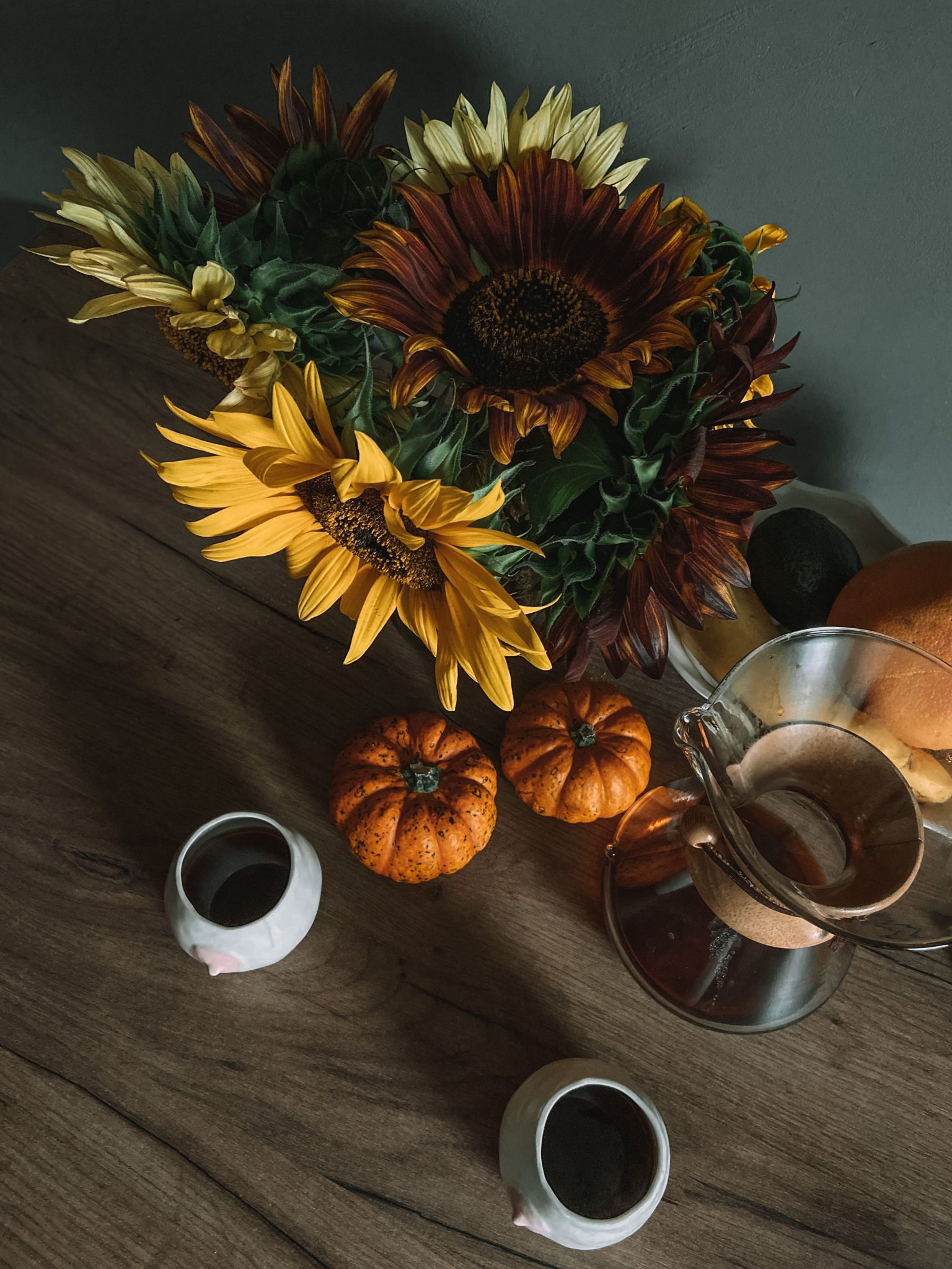 Aesthetic autumn setup featuring sunflowers, coffee, and pumpkins on a wooden table.