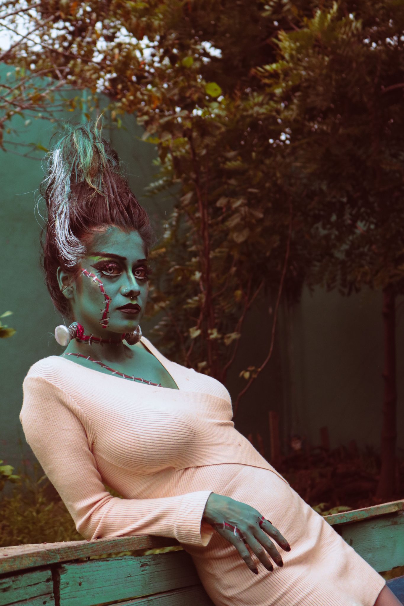 An artistic portrait of a woman in Halloween-themed makeup leaning outdoors.