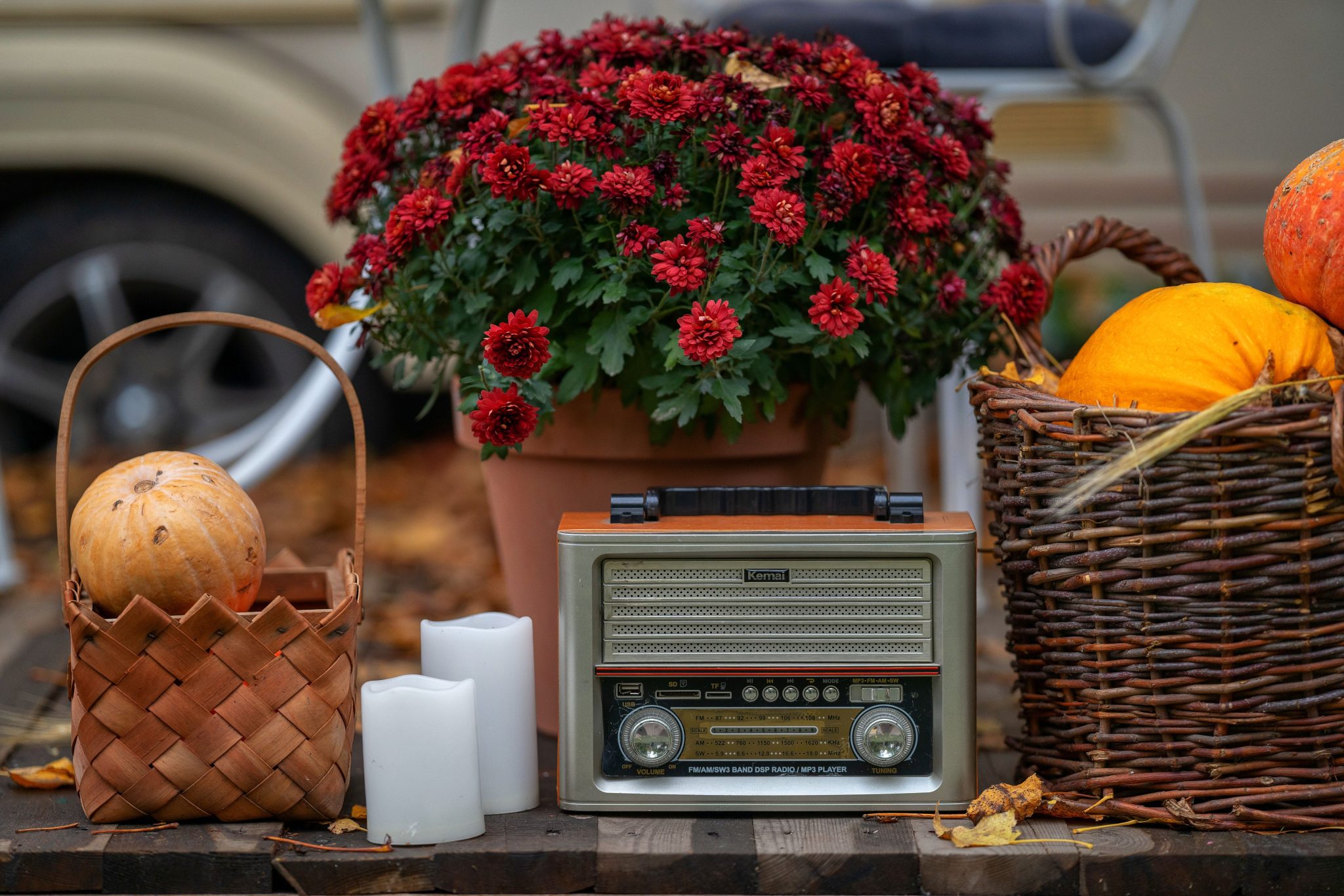 An autumn-themed still life featuring a vintage radio, pumpkins, baskets, and vibrant red flowers.