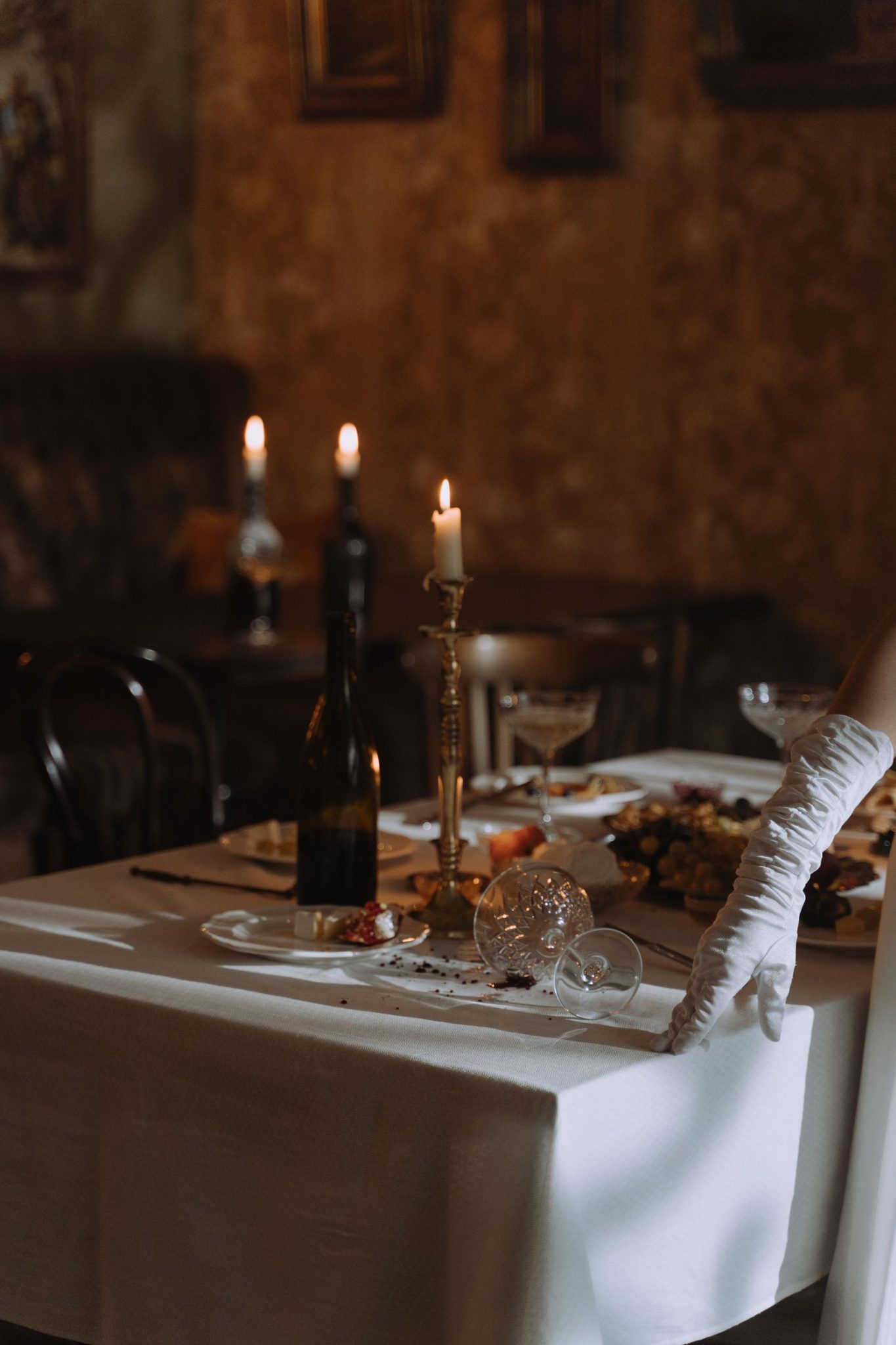 An elegantly set candlelit table with wine and intricate tableware creates a moody ambiance.