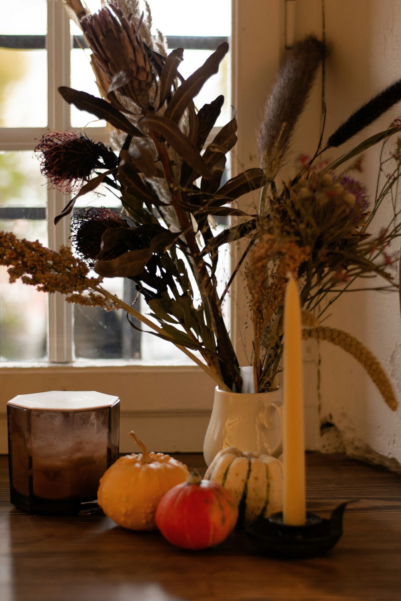 Autumn arrangement with pumpkins, dried flowers, and candle.